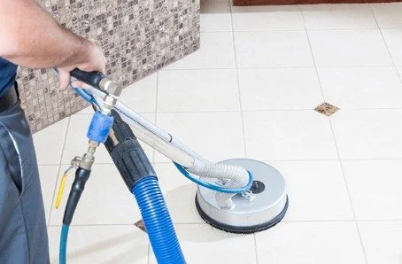 Person using a floor cleaning machine on a tiled floor.