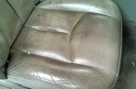 Close-up of a worn, leather car seat with visible cracks and stains.