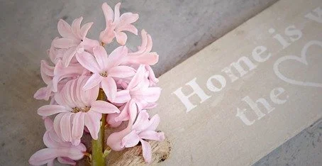 Pink hyacinth flowers next to a wooden sign that says 'Home is the'.