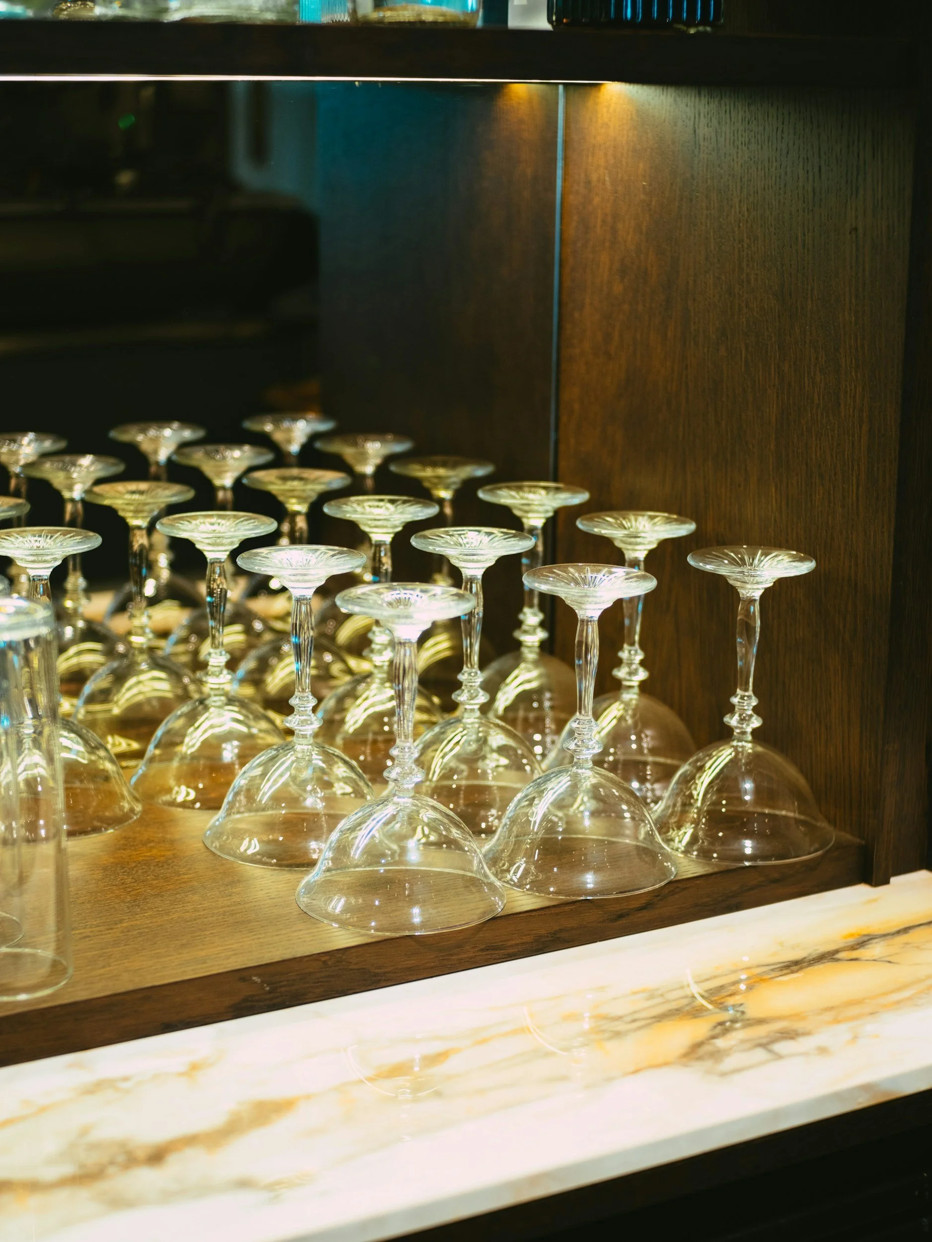A collection of upside-down martini glasses placed on a wooden shelf inside a bar or restaurant.