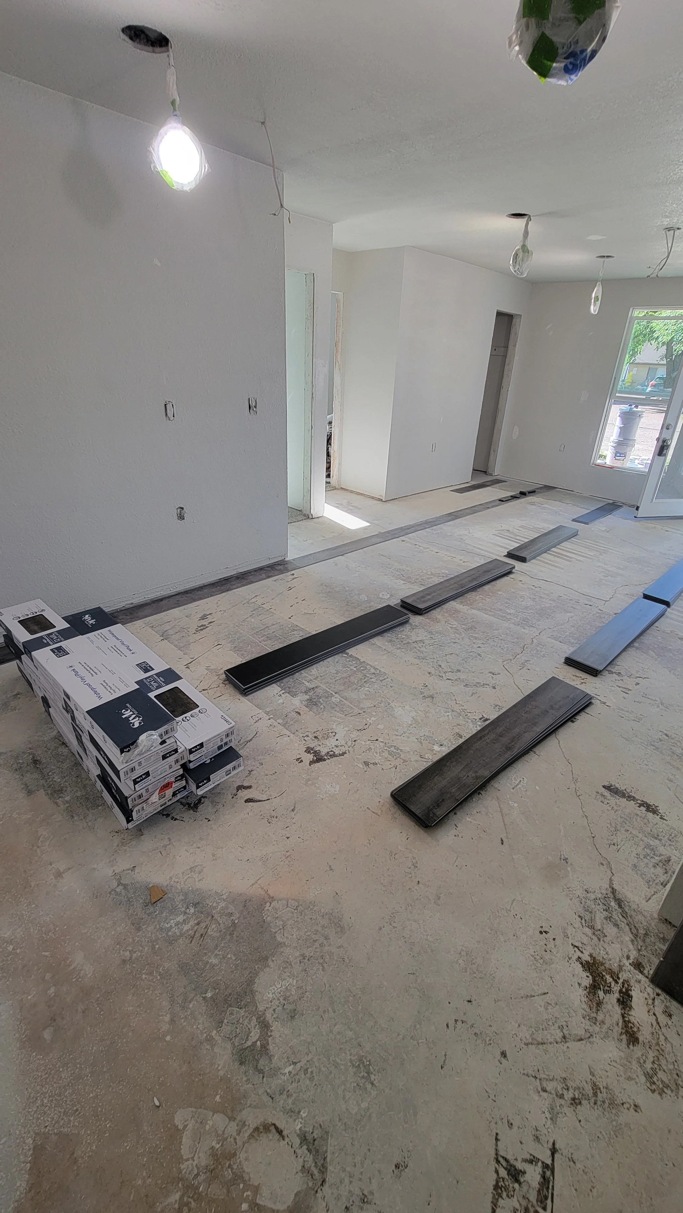 Interior of a house under renovation with flooring materials and subflooring partially installed, bare concrete floor, and unfinished white walls.