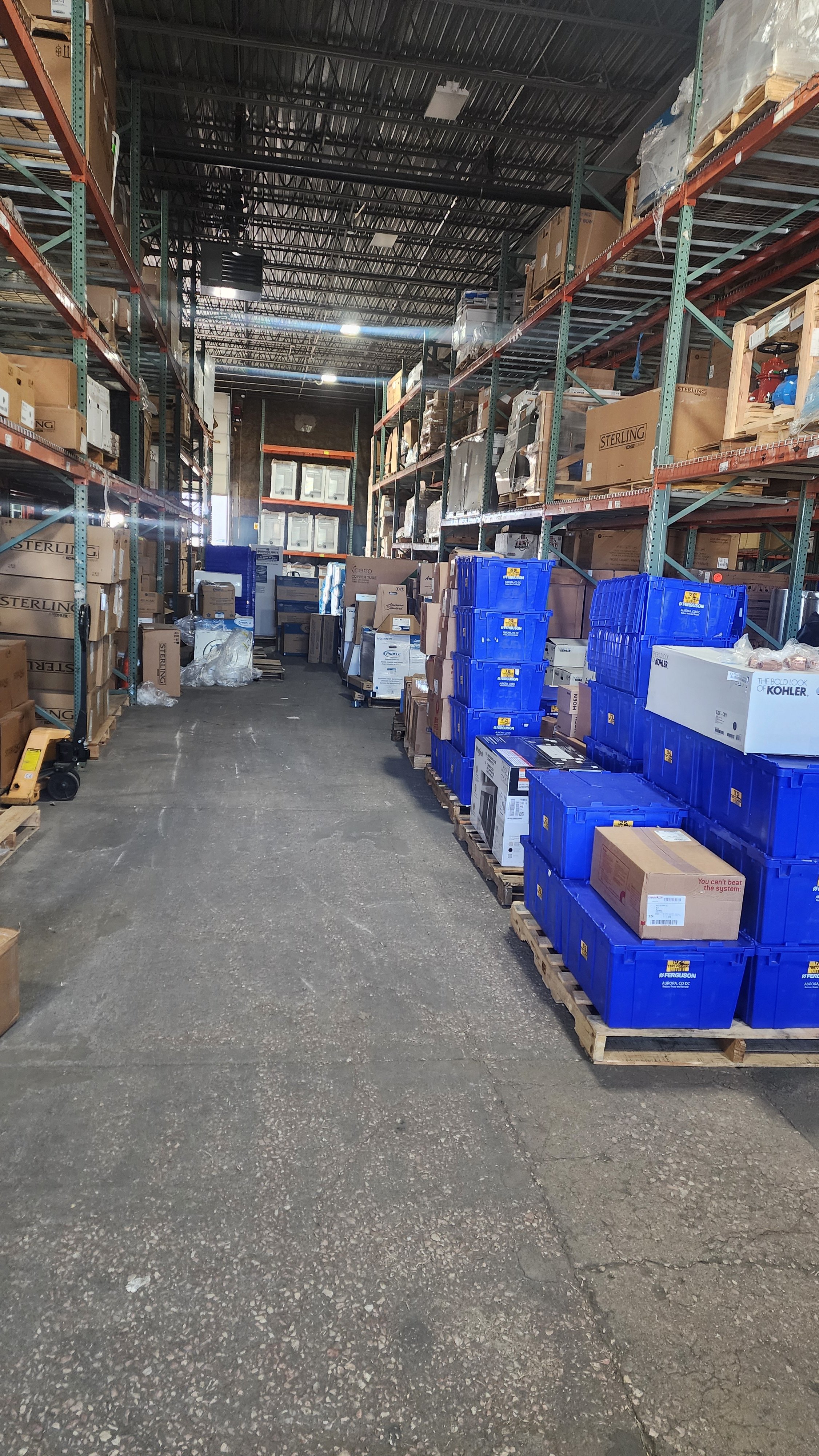 Warehouse aisle with shelving units filled with boxes and blue plastic containers on pallets.