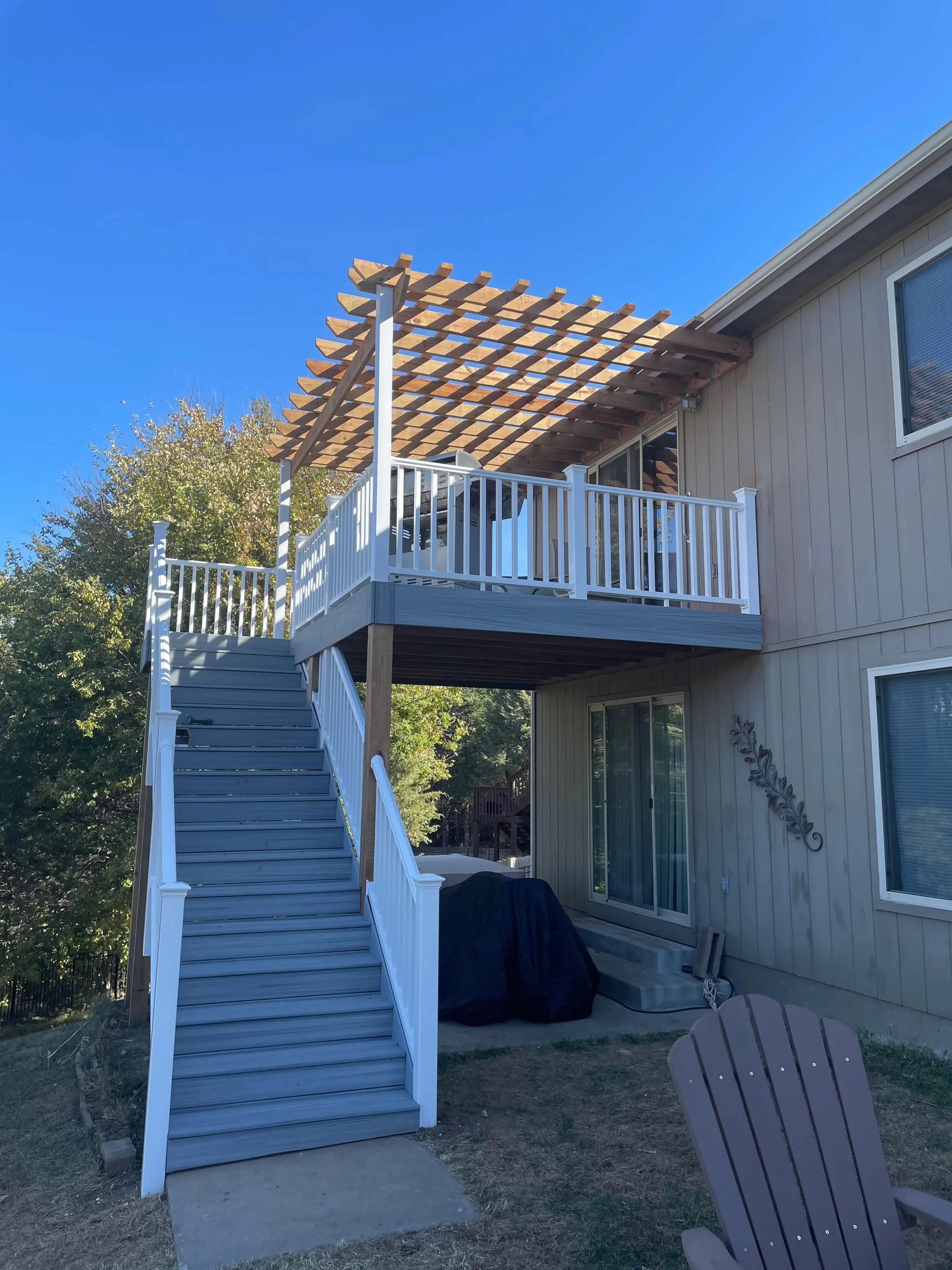 Backyard with a two-story wooden deck, stairs leading up to the upper level, a patio table with chairs, and a bright blue sky.