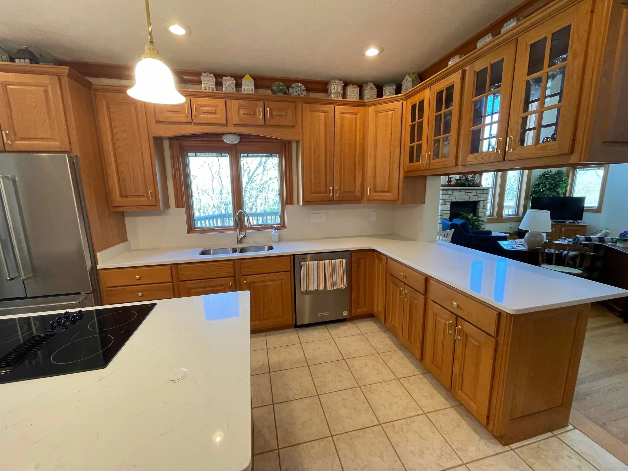 Kitchen with wooden cabinets, white countertops, stainless steel stove and dishwasher, window above sink, and view into living room with fireplace and TV.