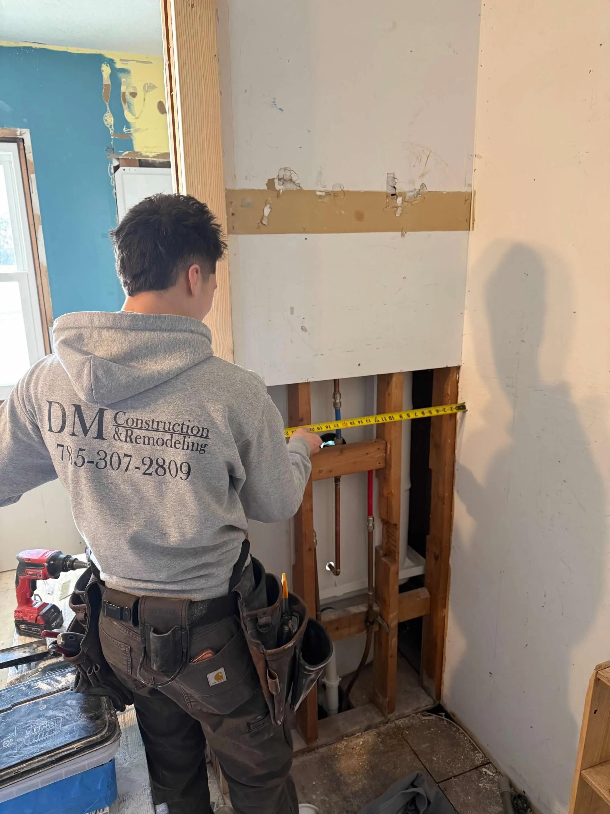 A construction worker in a gray hoodie measuring the wall with a tape measure during renovation.