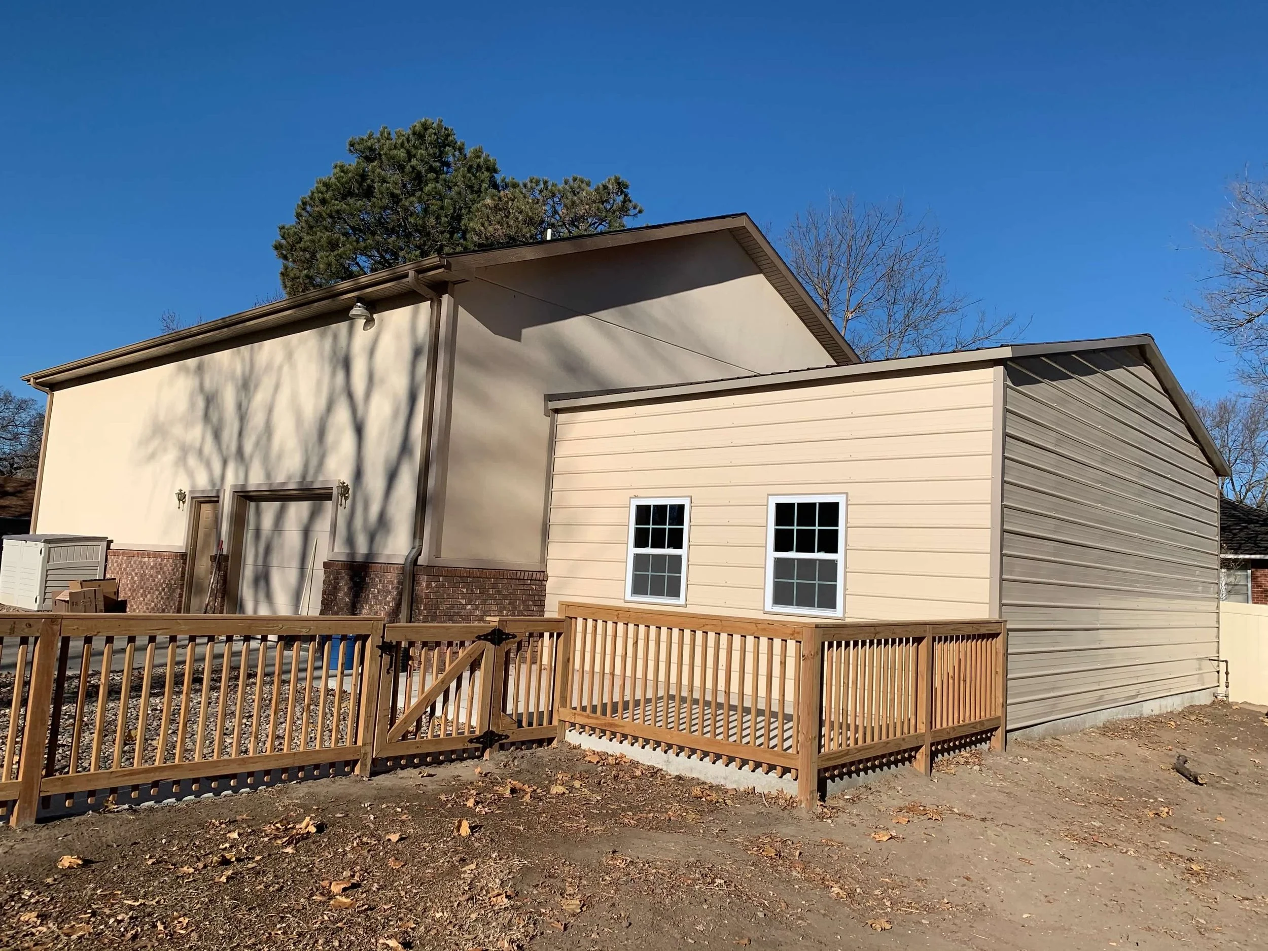 An exterior view of a house with a new small wooden deck, beige siding, and two windows, under a clear blue sky.