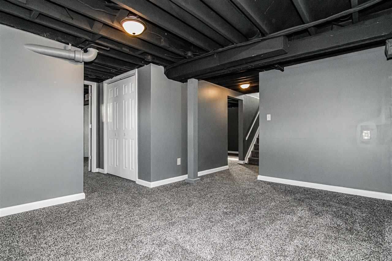 Empty finished basement with gray walls, gray carpet, and exposed black ceiling with lighting fixtures.