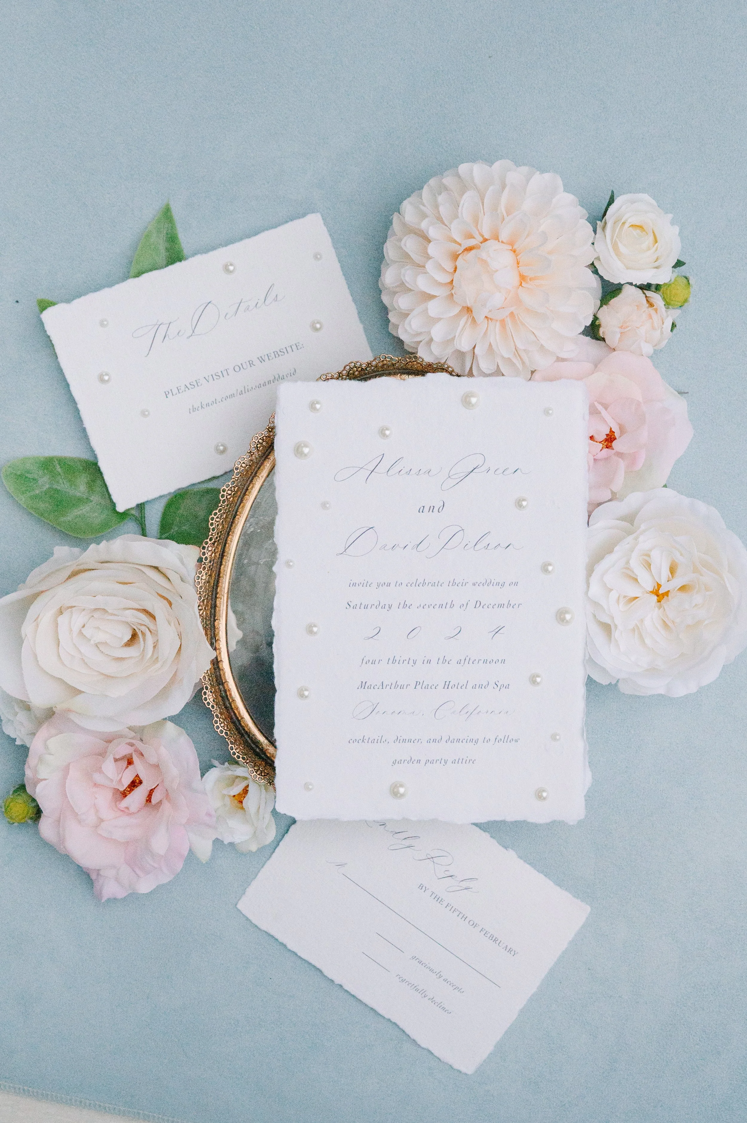 Wedding invitation with flowers and pearl decorations, surrounded by pink and white flowers and green leaves.