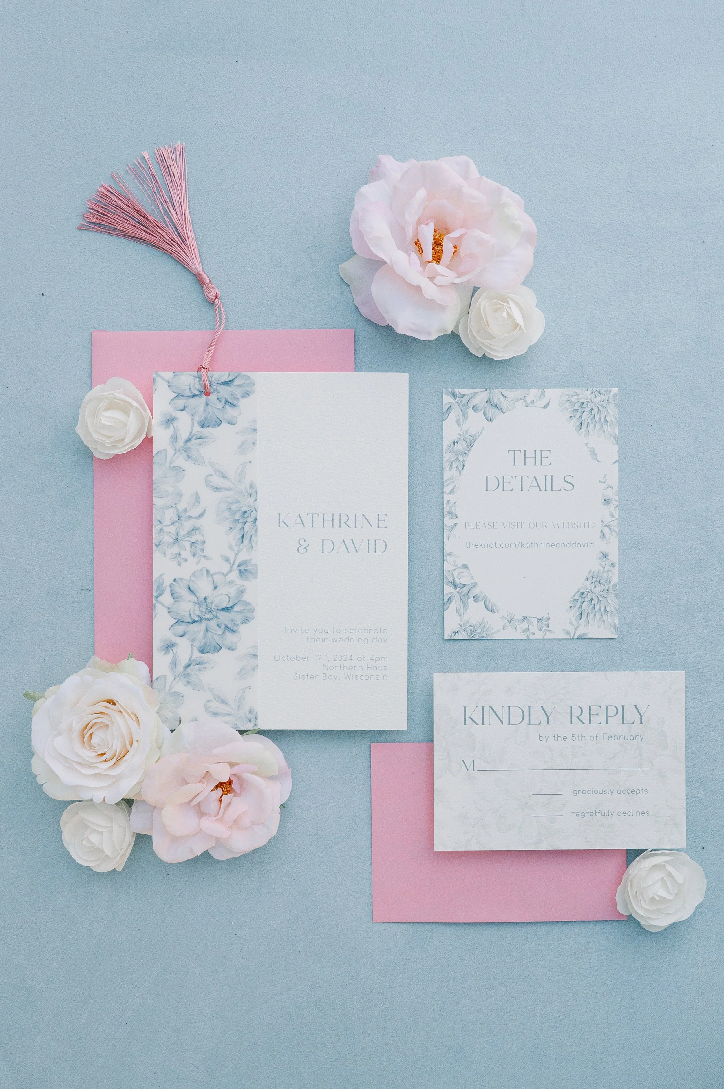 Wedding invitation suite with floral accents and pink and white flowers on a light blue background.