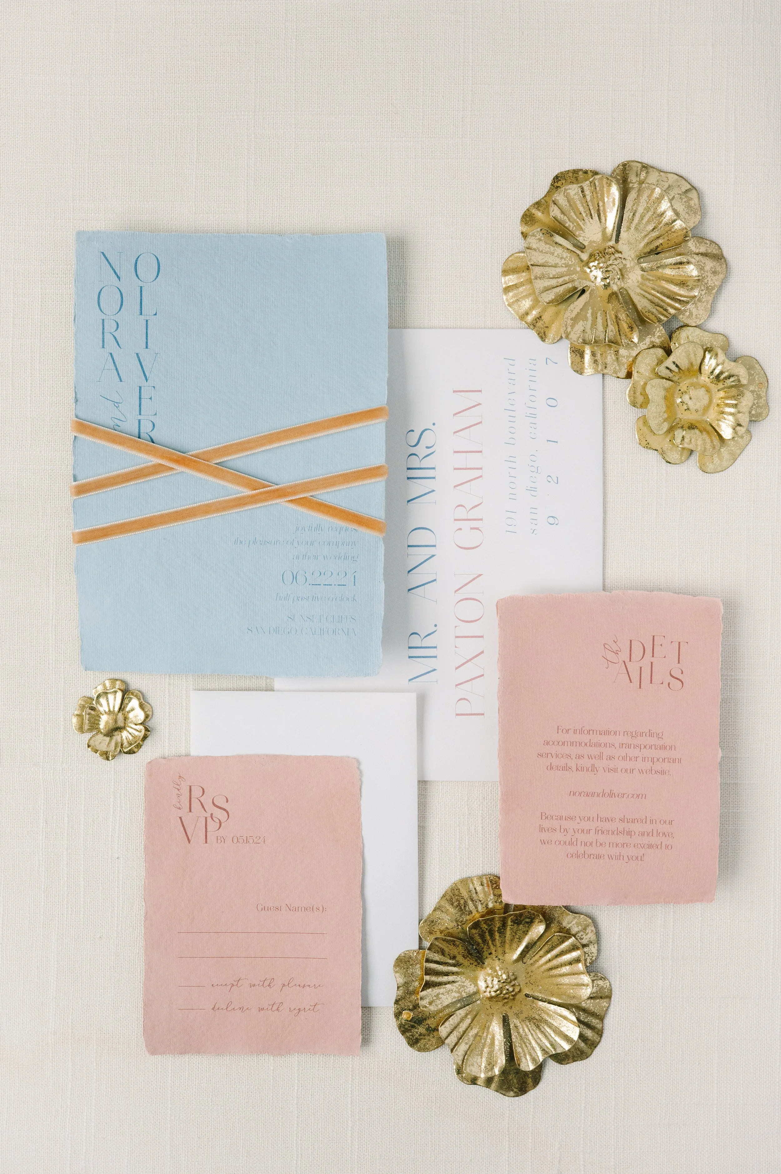 Invitation suite for a wedding with gold floral accents, pink and blue RSVP cards, and light-colored paper.