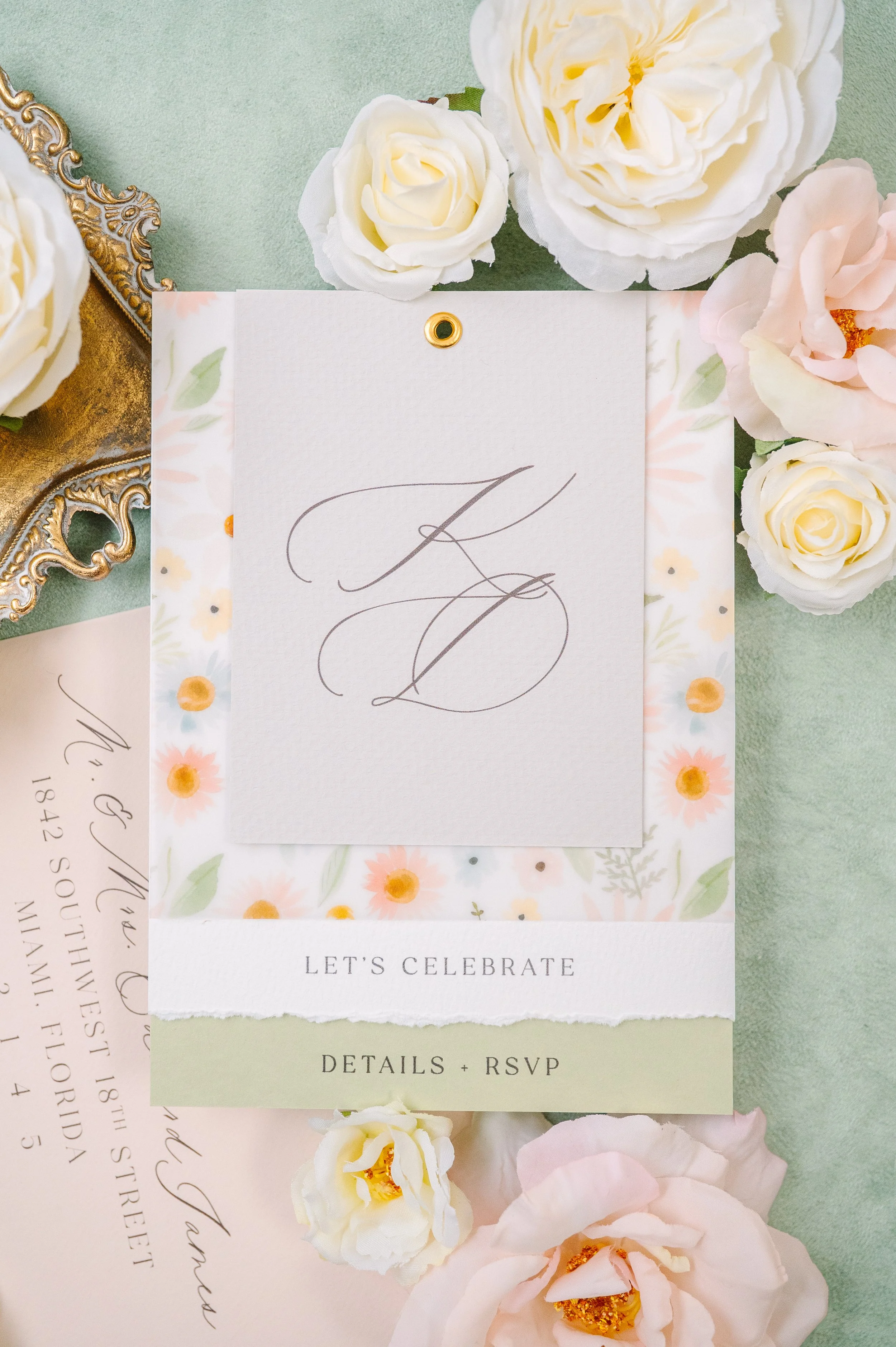 A wedding or celebration invitation surrounded by white, pink, and cream-colored flowers on a light green background.