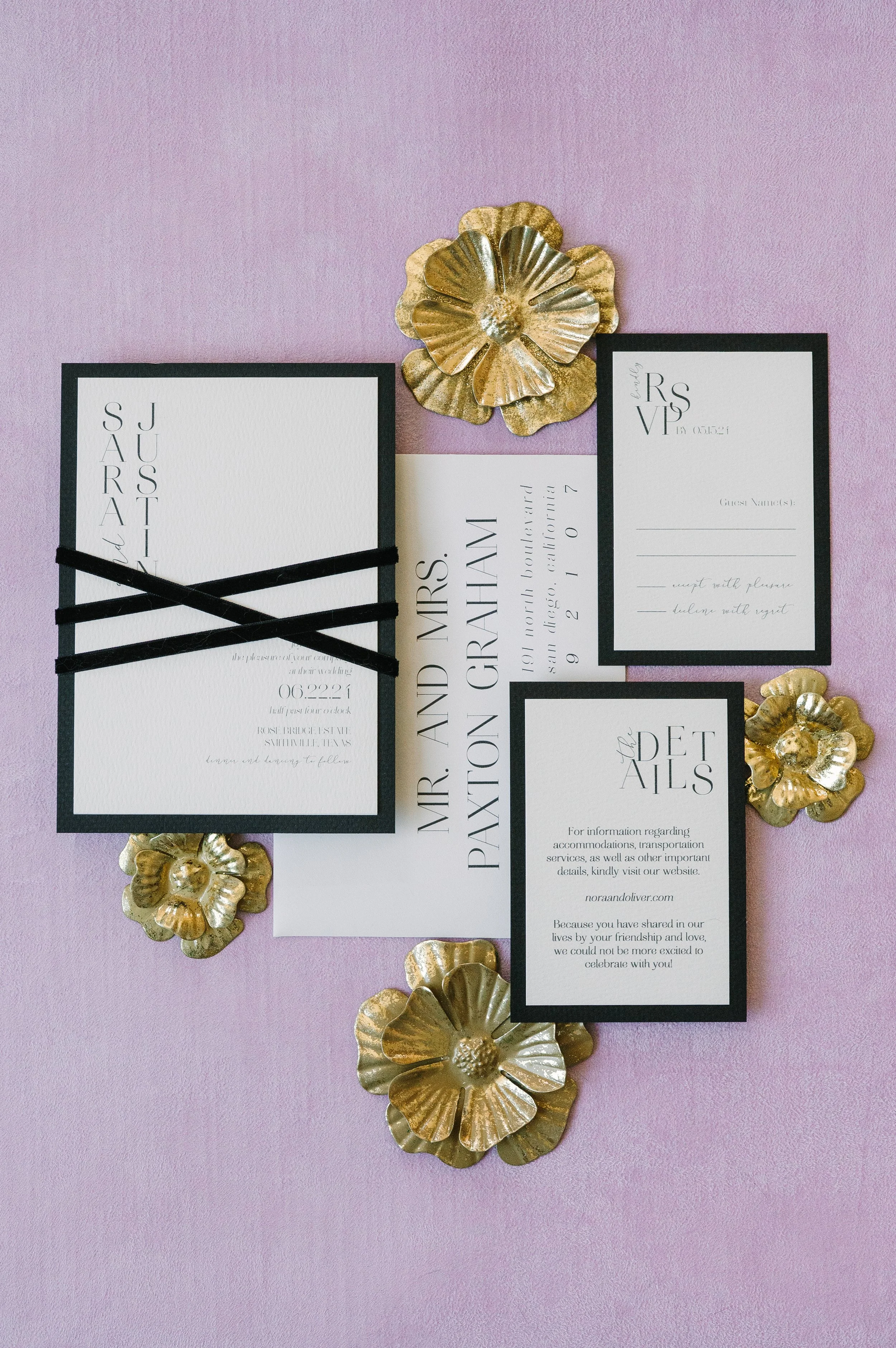 Wedding invitation suite with black and white cards, gold floral accents, and a lavender background.