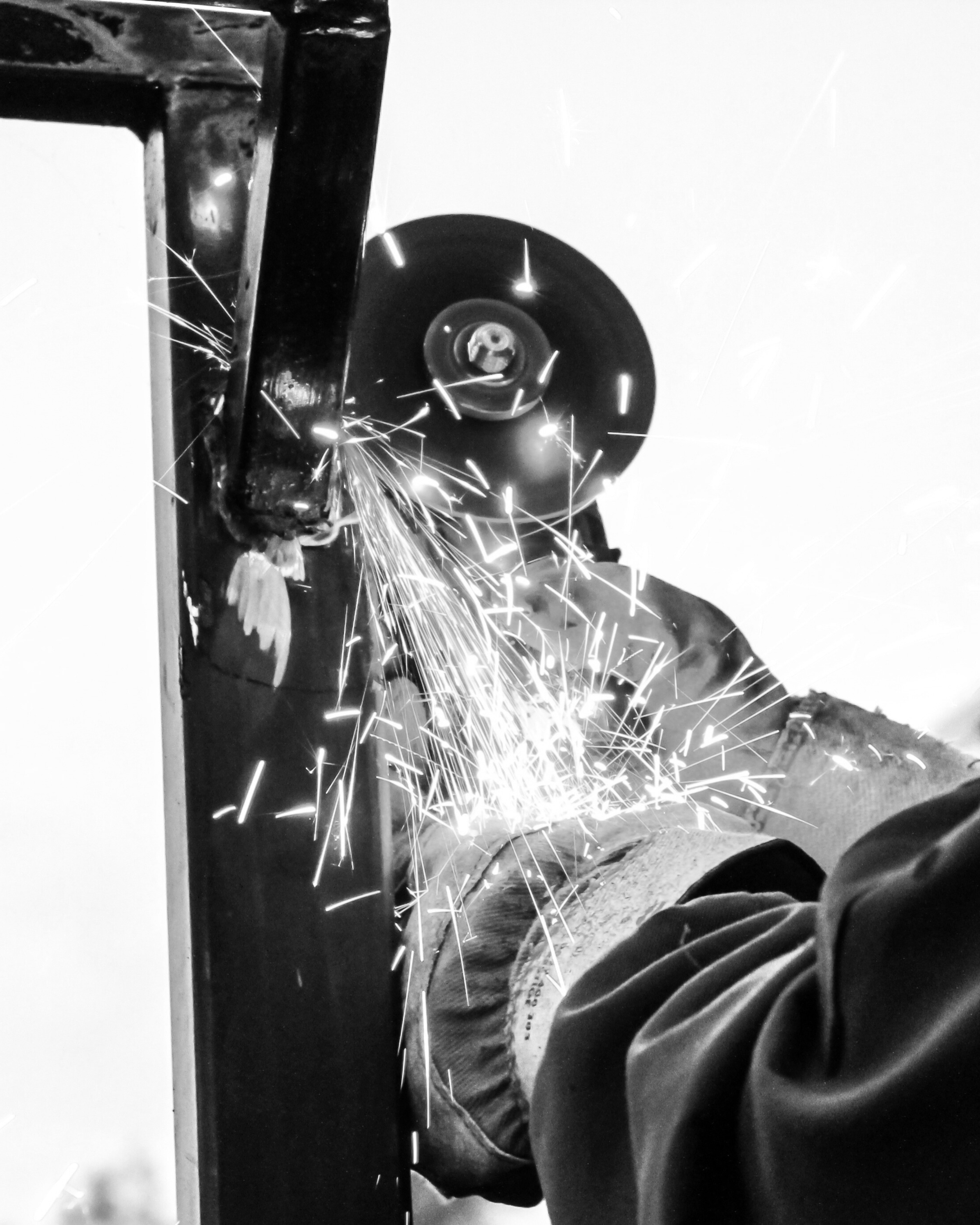 A person using an angle grinder to cut or grind a metal pipe, with sparks flying.
