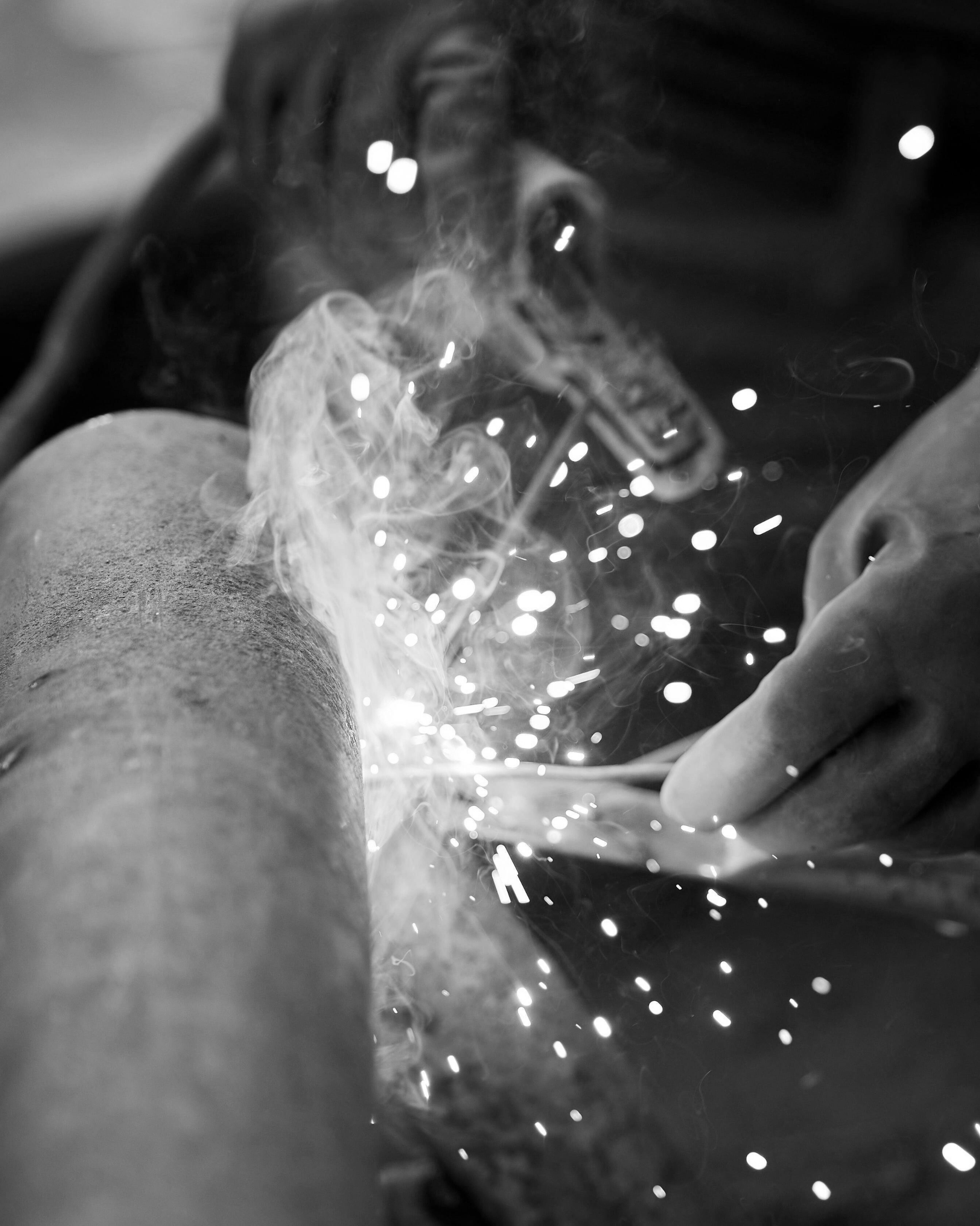 A person welding metal, sparks and smoke flying as they work on a surface in an industrial setting.