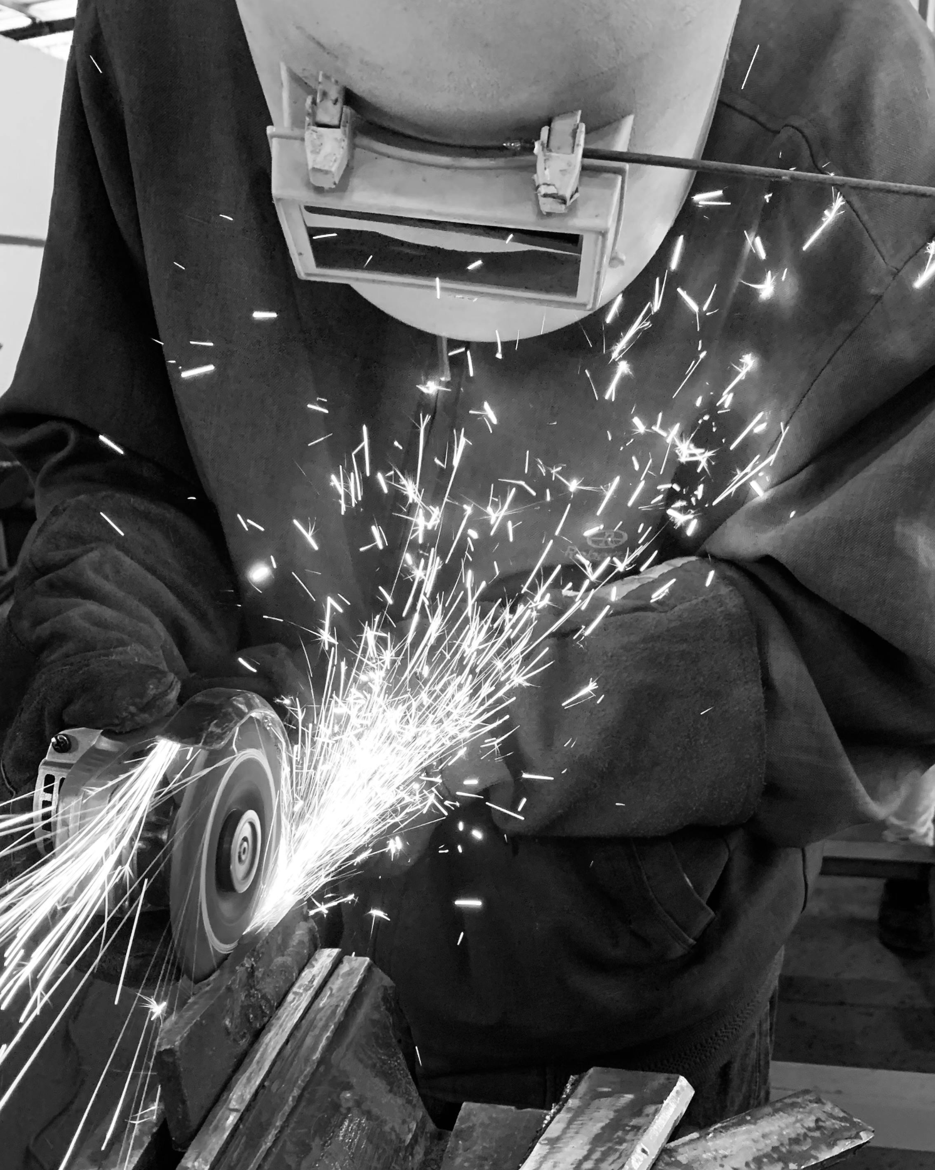 A person using an angle grinder to cut metal, with sparks flying in a workshop setting.