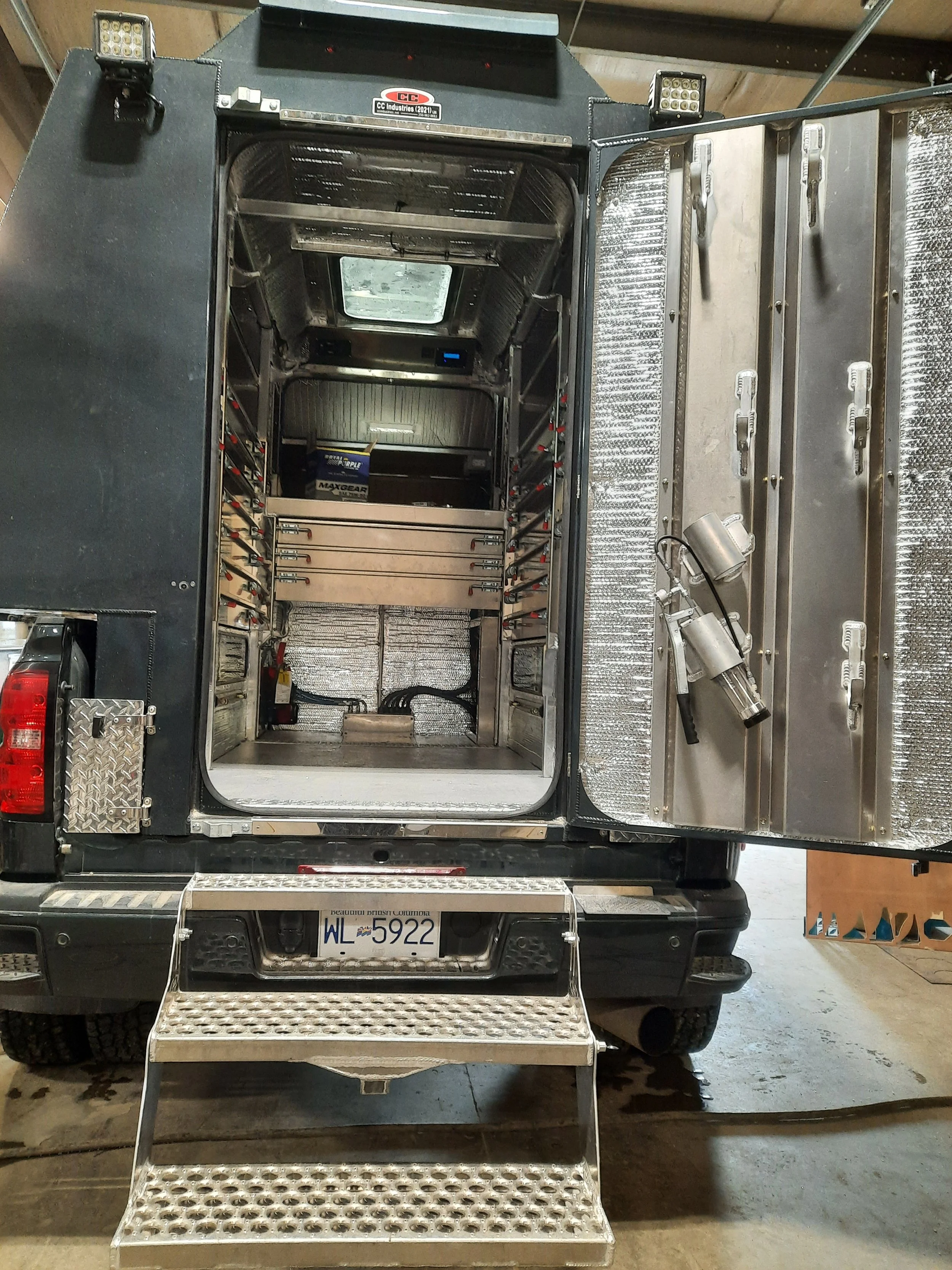 Back of a truck with the rear open, showing empty compartments and equipment inside, with a step ladder at the bottom.