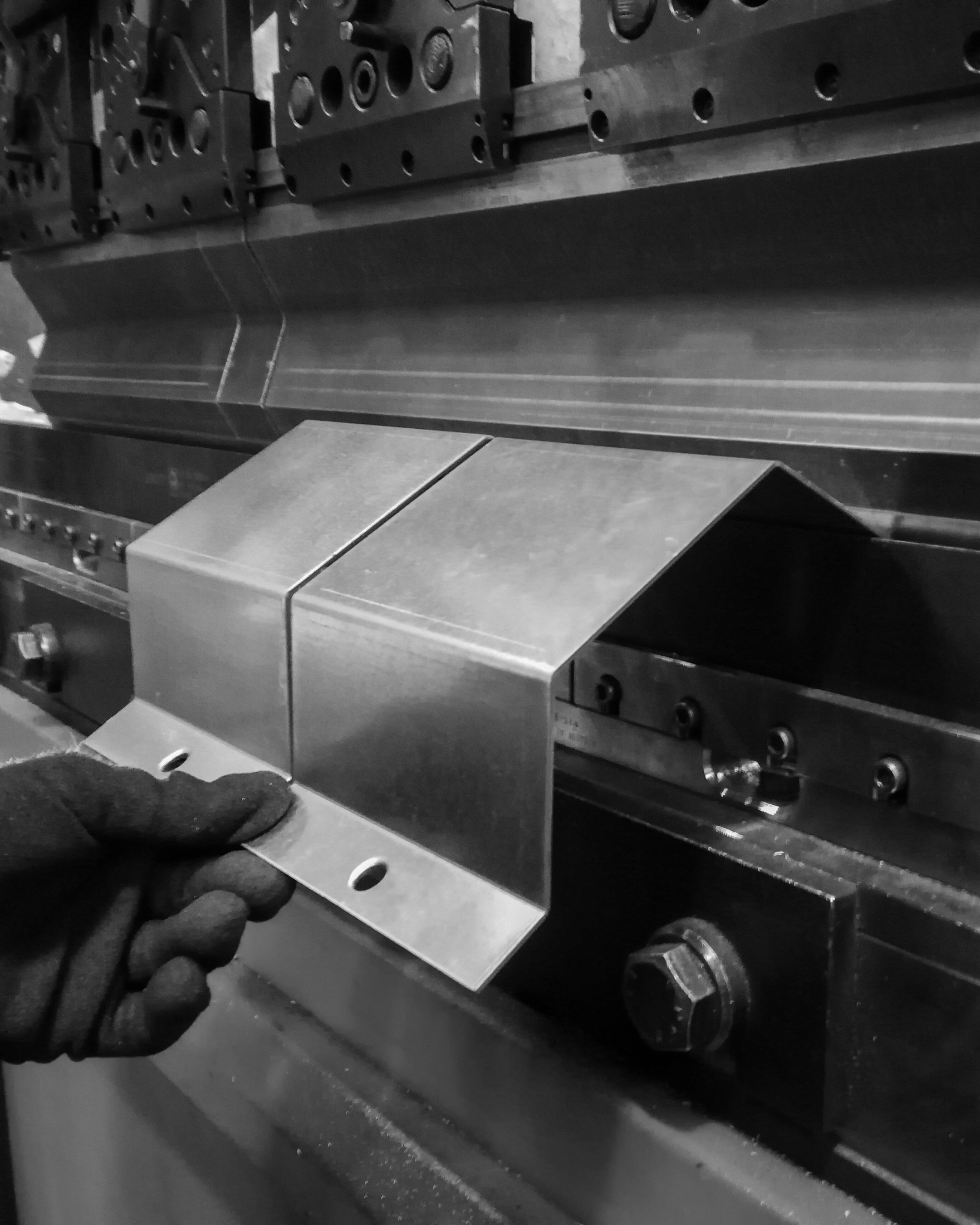 A person wearing a glove holding sheet metal being bent by a metal bending machine in a shop.