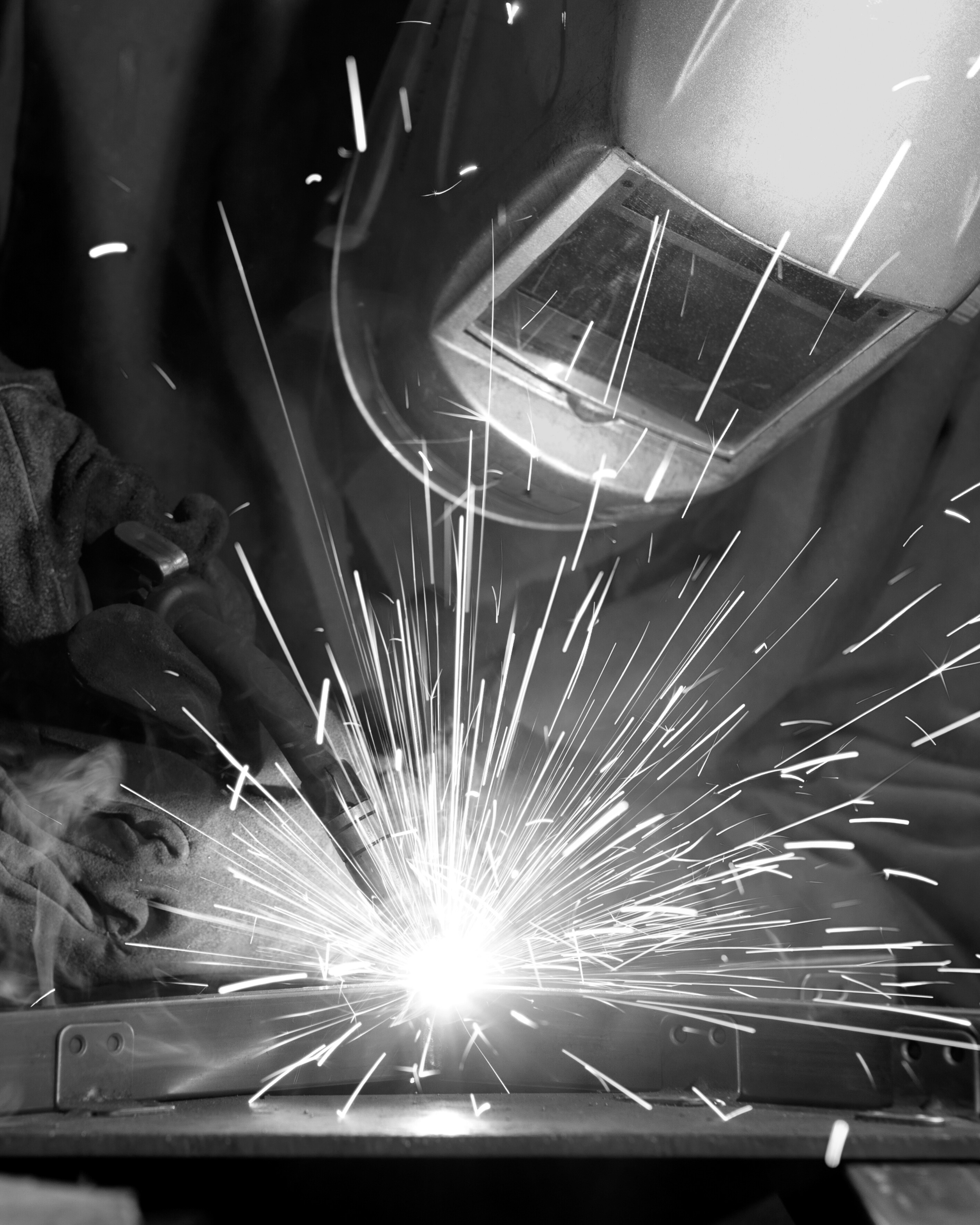 A person welding metal, with sparks flying in different directions, wearing protective gloves and a welding helmet.