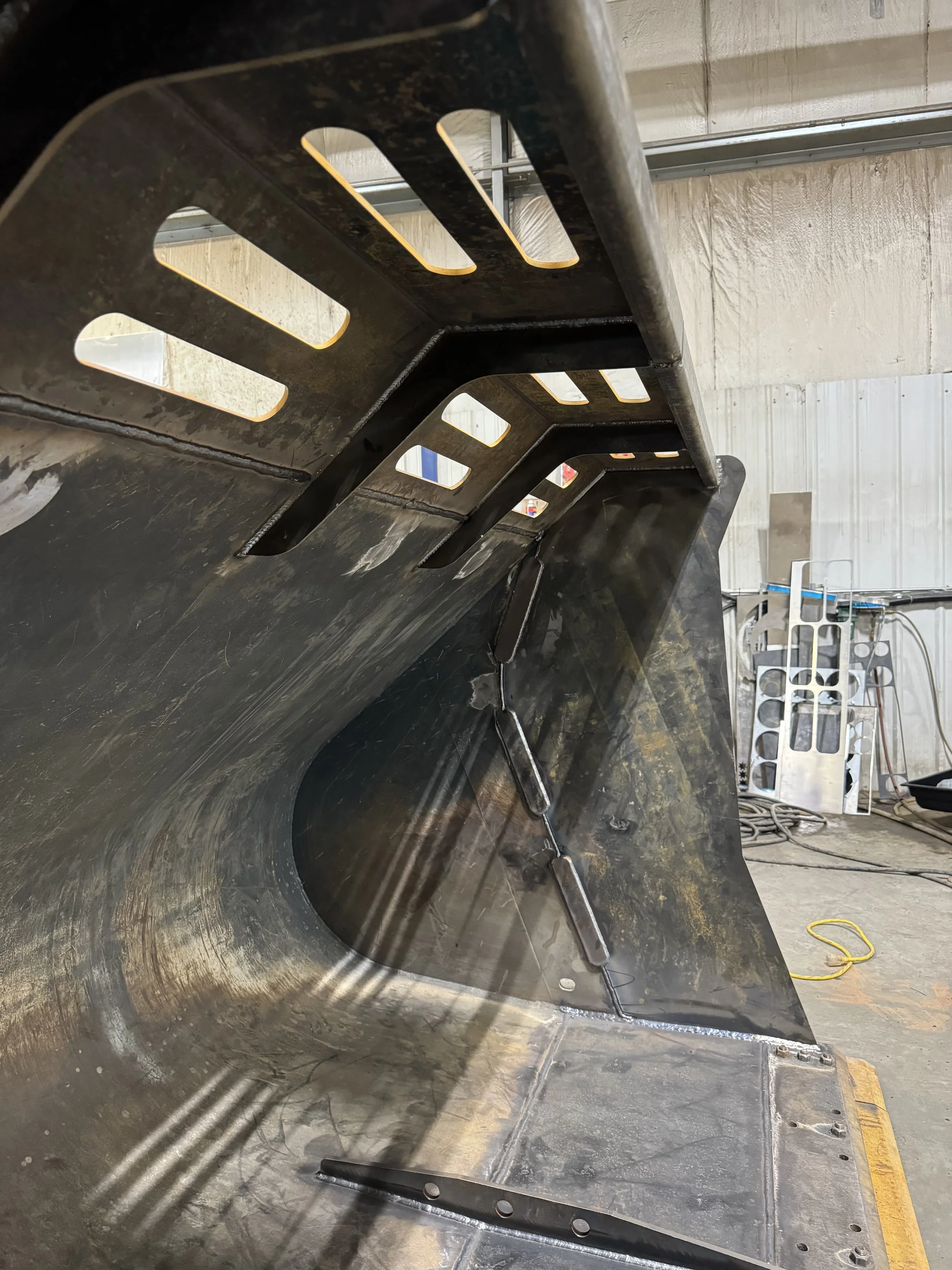 Close-up view of the interior of a large industrial metal container or machinery part, showing metal panels, welded joints, and cutout slots, likely in a manufacturing or workshop setting.