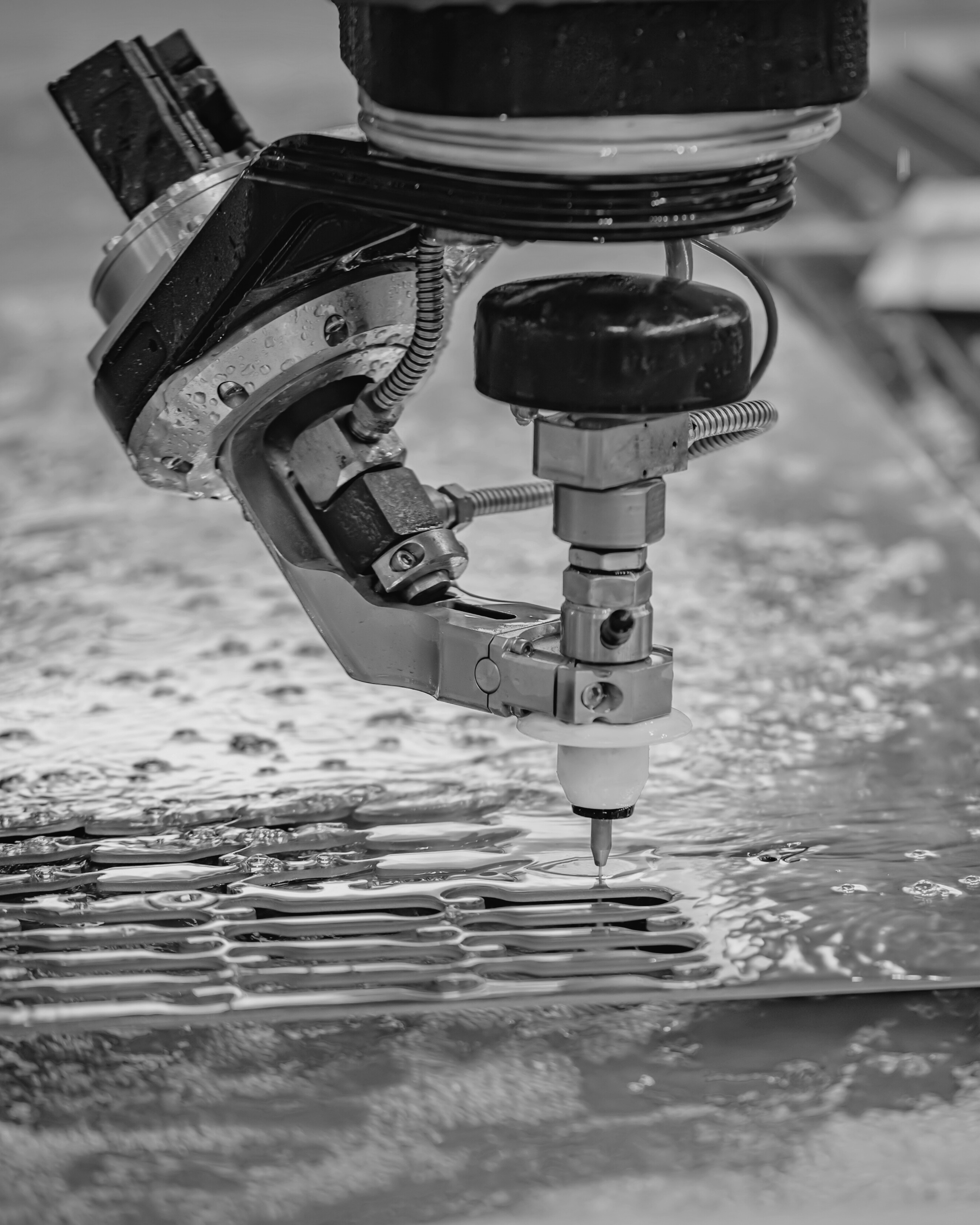 Close-up of a robotic water jet cutter engraving a metal surface with water and abrasive material.
