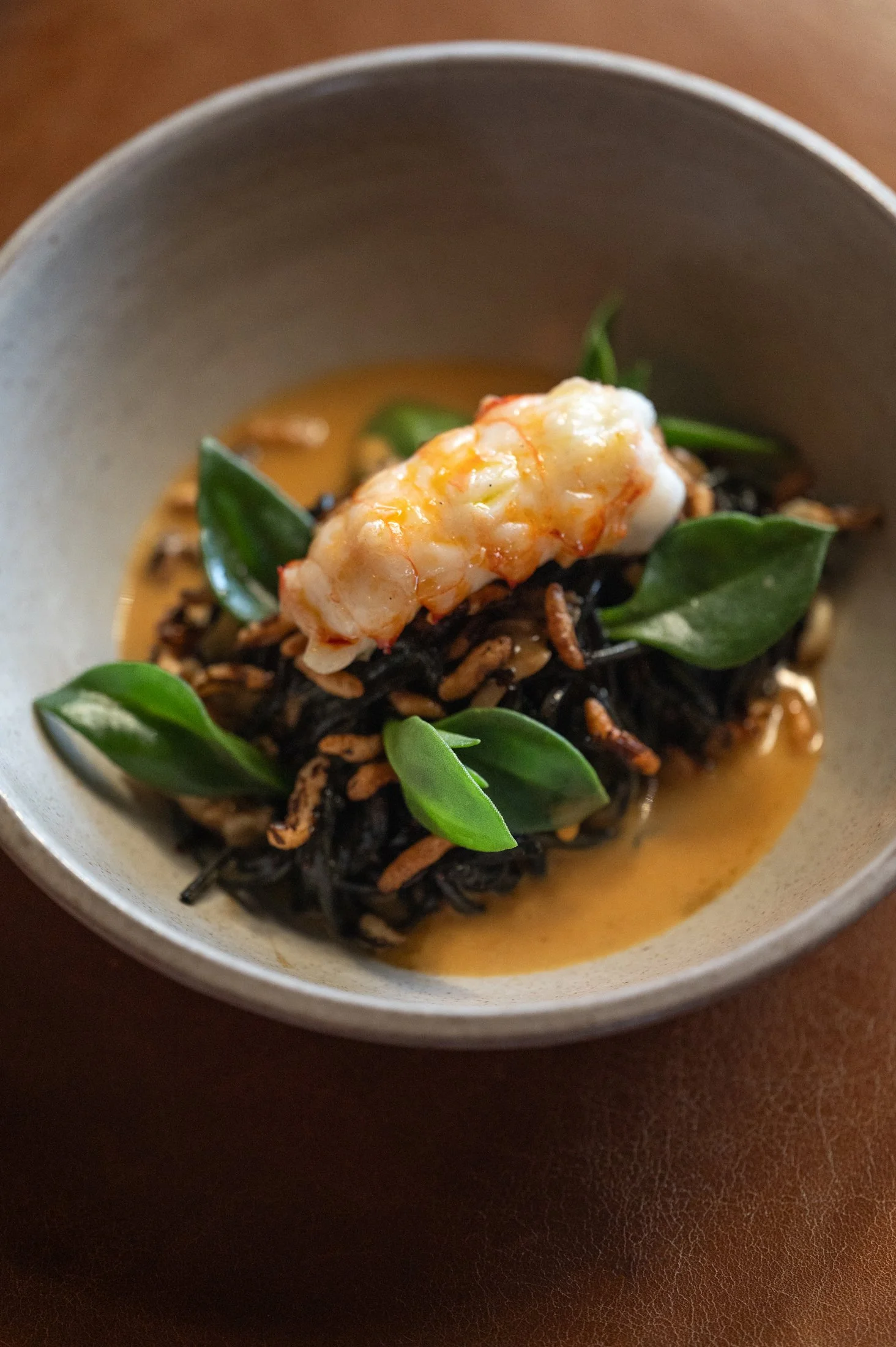 A bowl containing a seafood dish with shrimp, green leaves, and a creamy orange sauce.