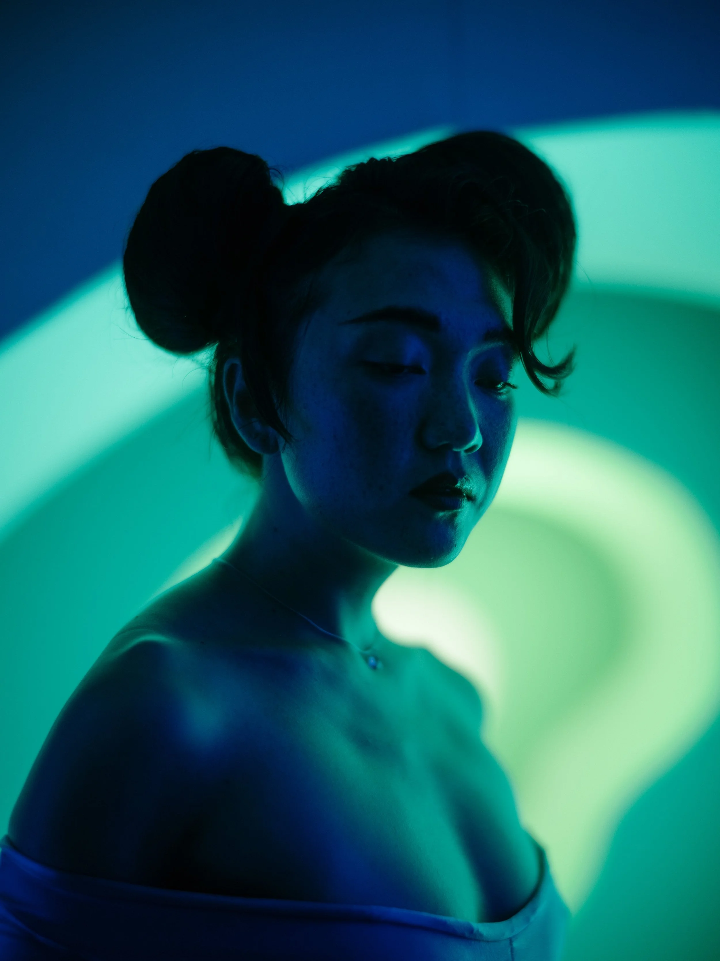 Profile of a woman with two buns hairstyle, illuminated by blue and green lighting, with her eyes closed.