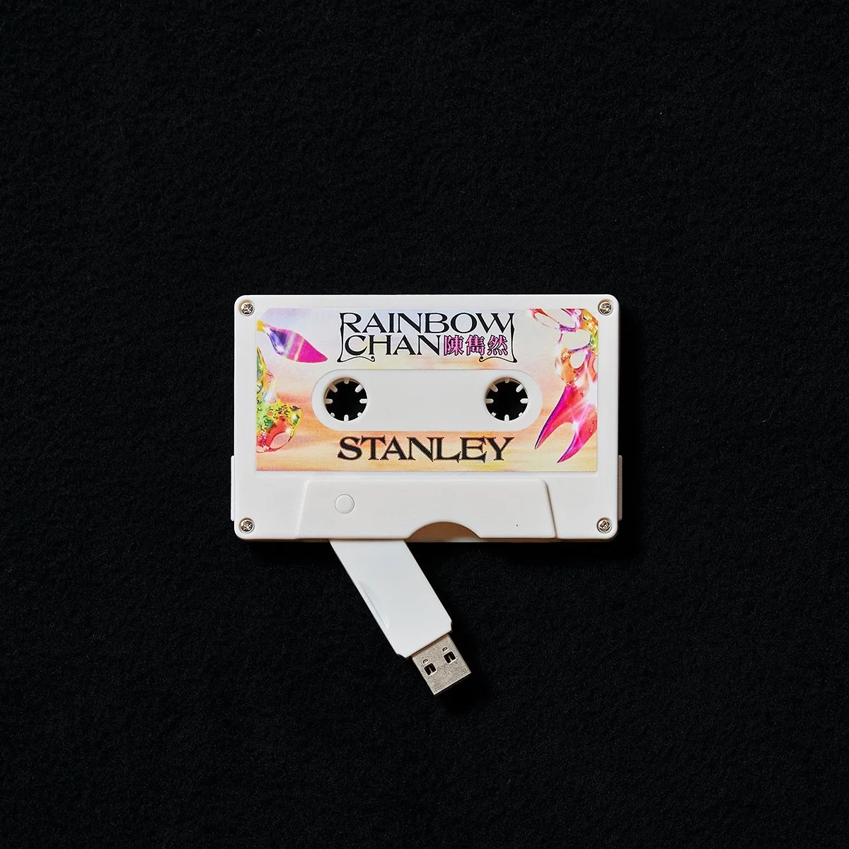 A cassette tape with a colorful label that says 'Rainbow Chan' and 'Stanley', placed on a black background.