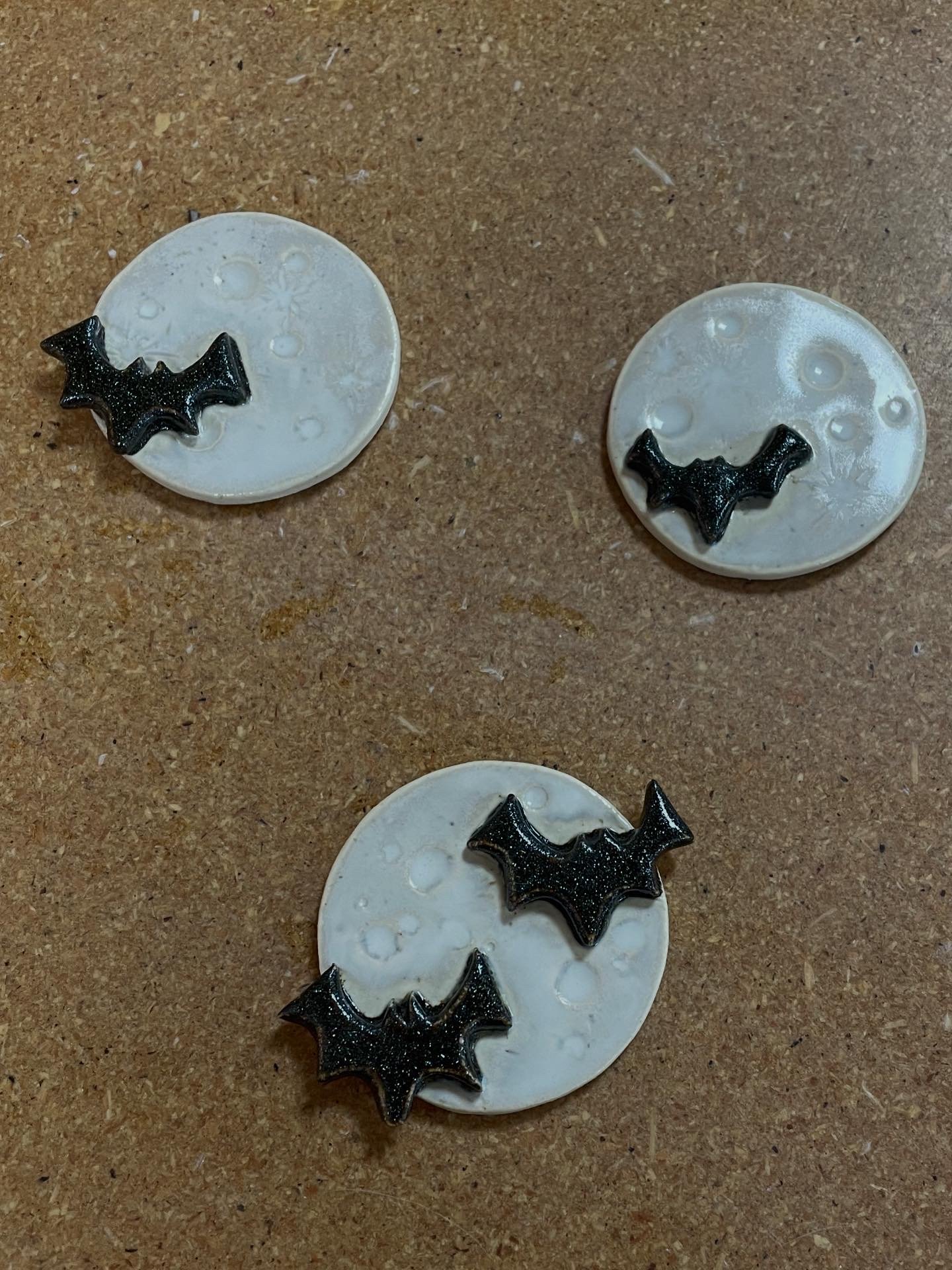 Three moon magnets, each with black bat-shaped decorations, on a brown table.