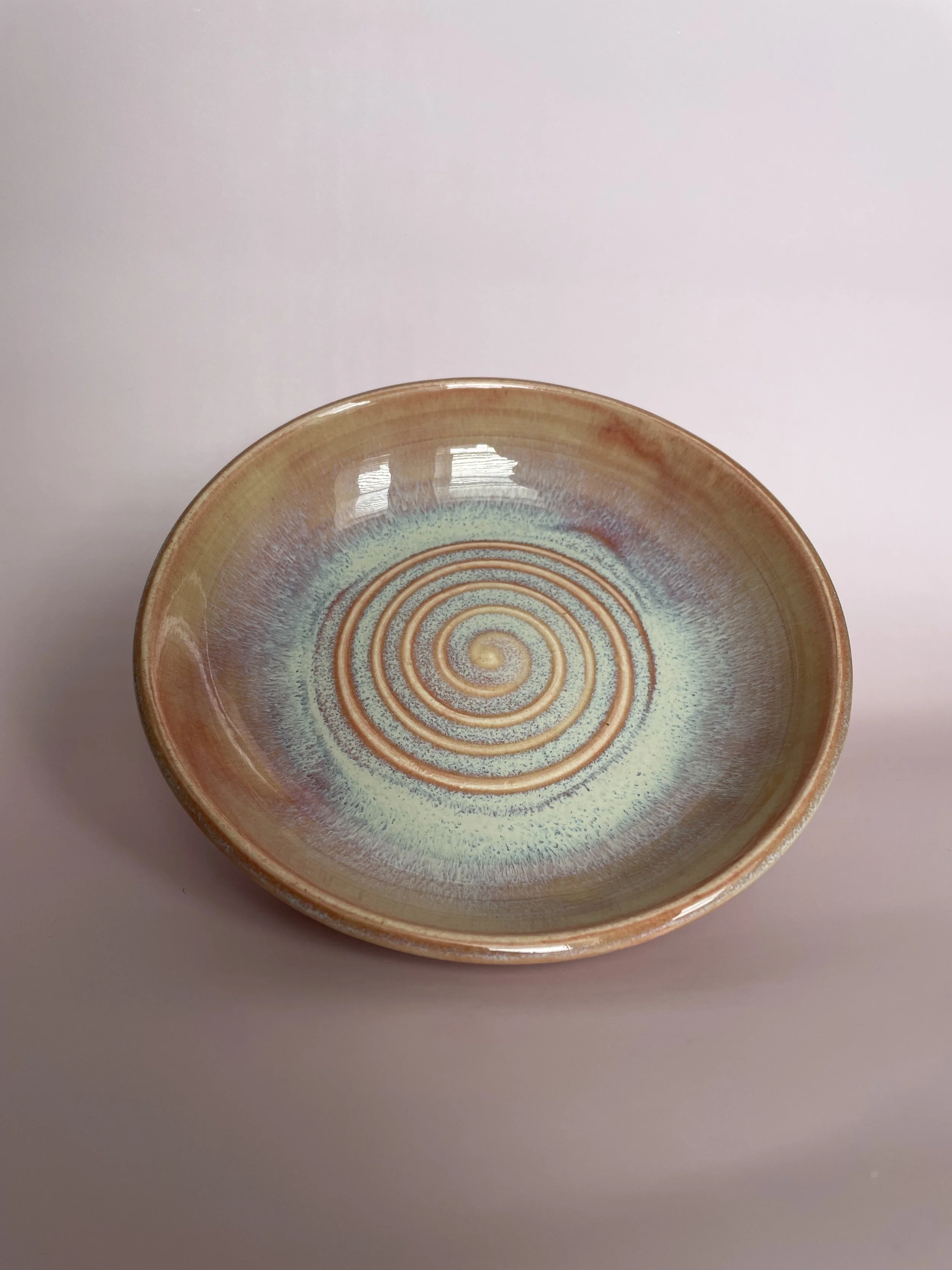 Decorative ceramic bowl with a spiral pattern and glazed in pink and blue tones.