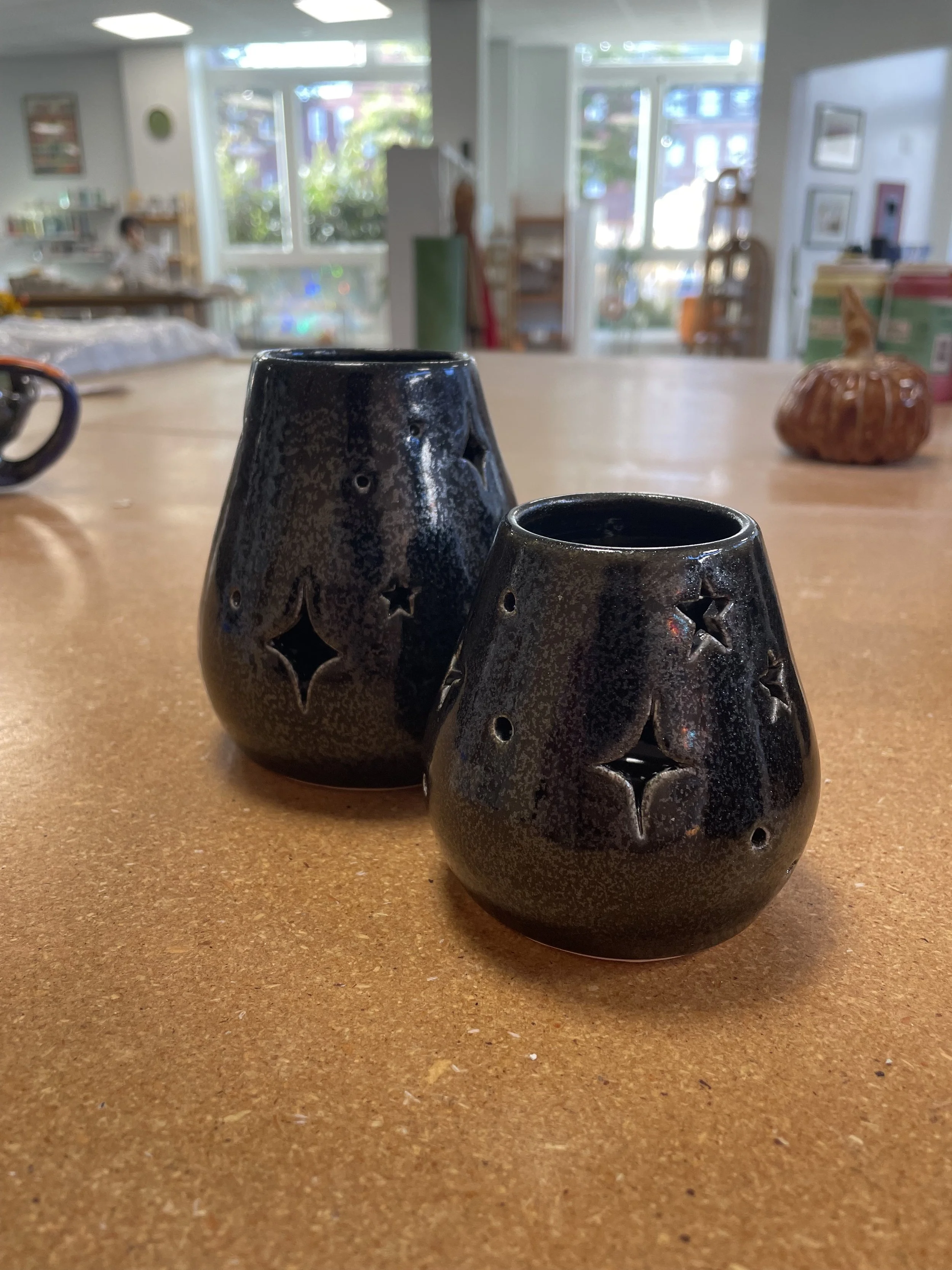 Two black ceramic candle holders with star and moon cutouts on a wooden table inside a bright room.