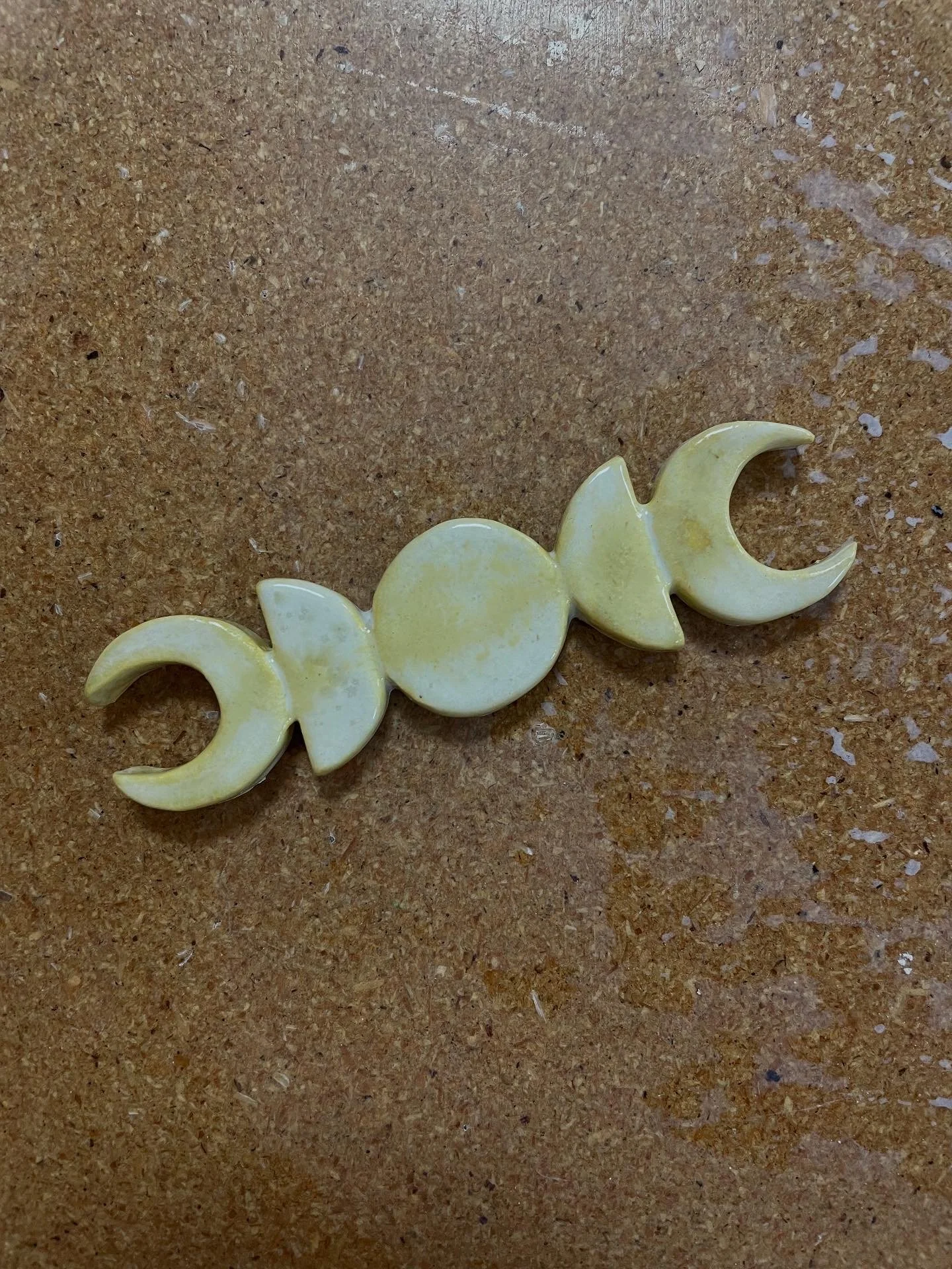 A small decorative magnet with a various moon phases, all in a pale yellow color, placed on a brown table.