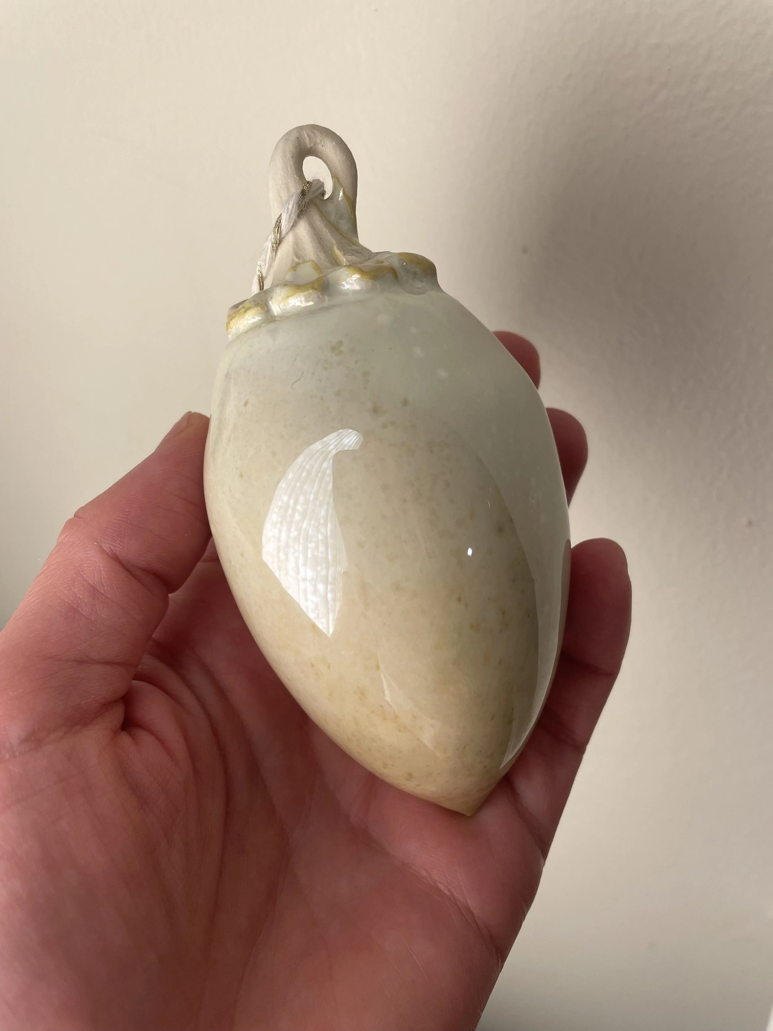 A photograph of a ceramic heart-shaped sculpture with a swan on top, held in a person's hand against a plain wall background.