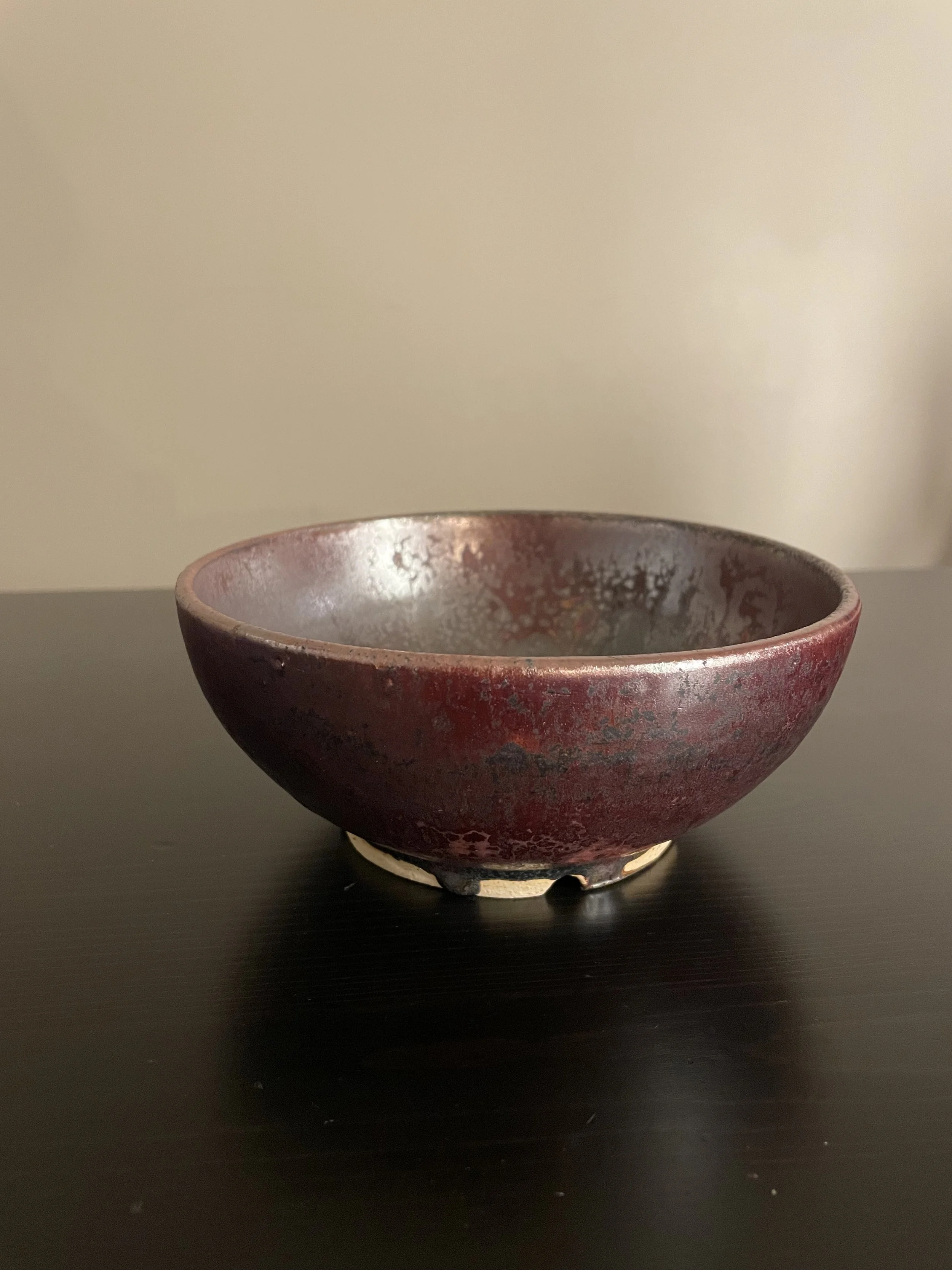A round red ceramic bowl with a slightly textured surface, sitting on a black surface against a plain beige background.