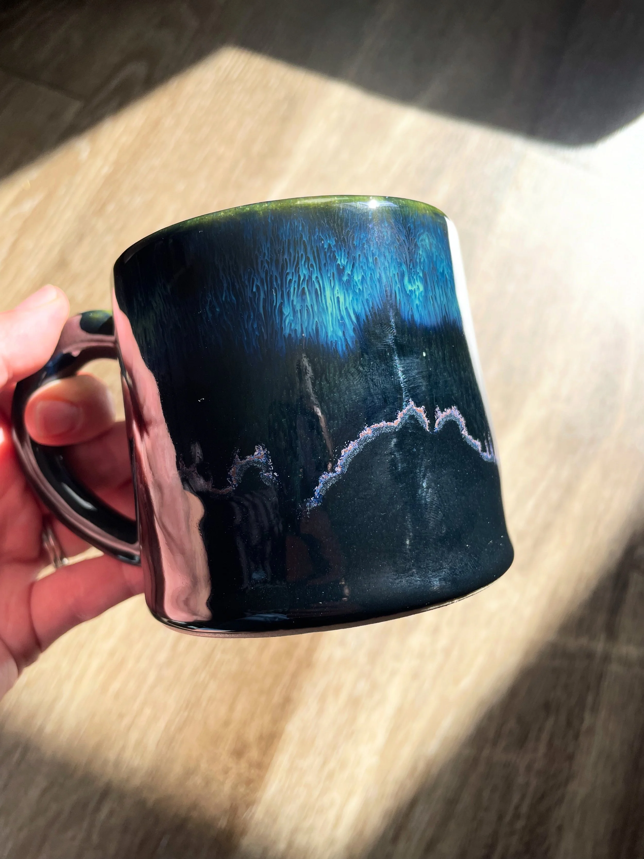 A ceramic mug with a mountain landscape and Aurora Borealis design.