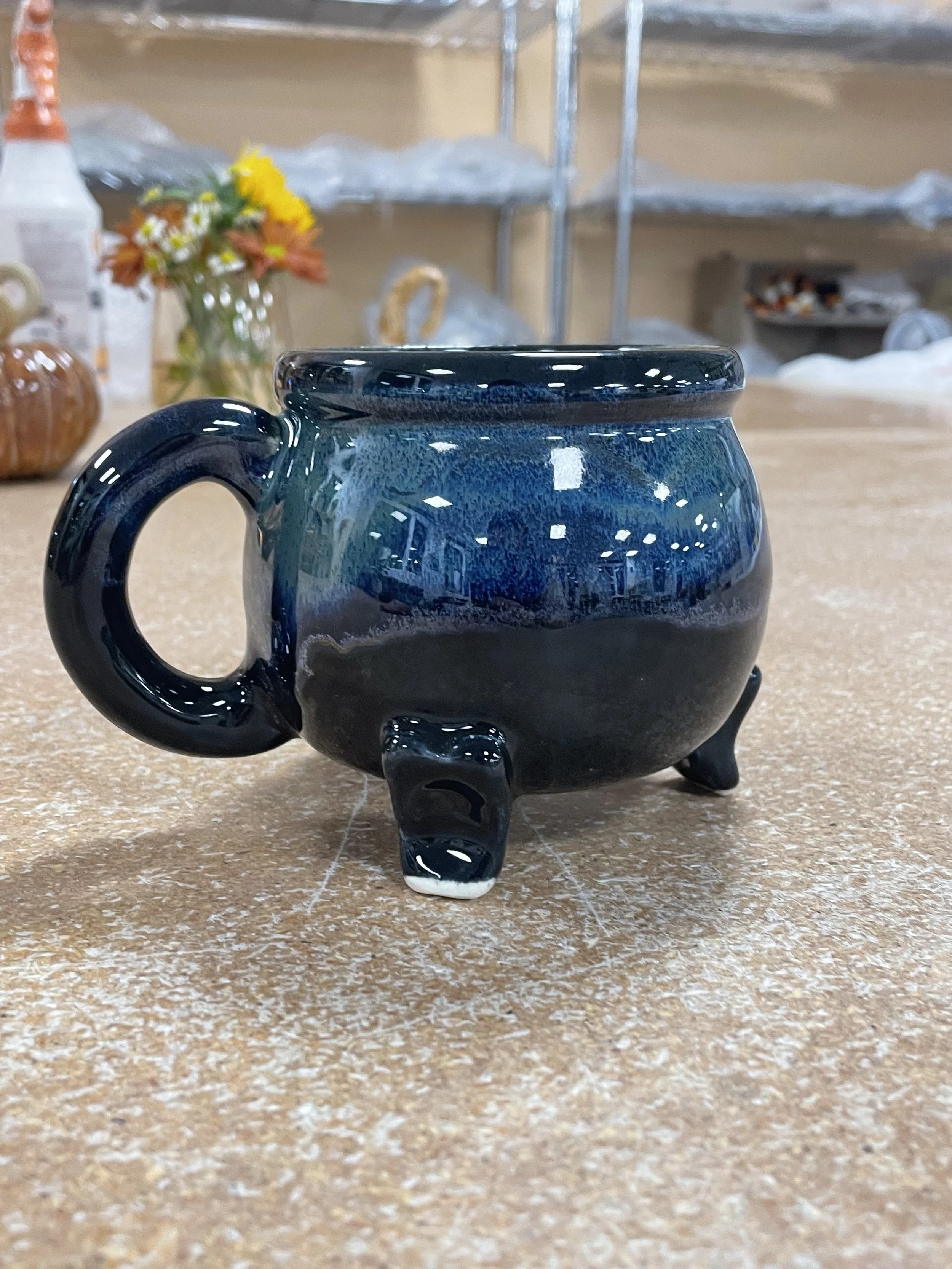 A small, black and blue glazed ceramic cauldron mug on a brown table.