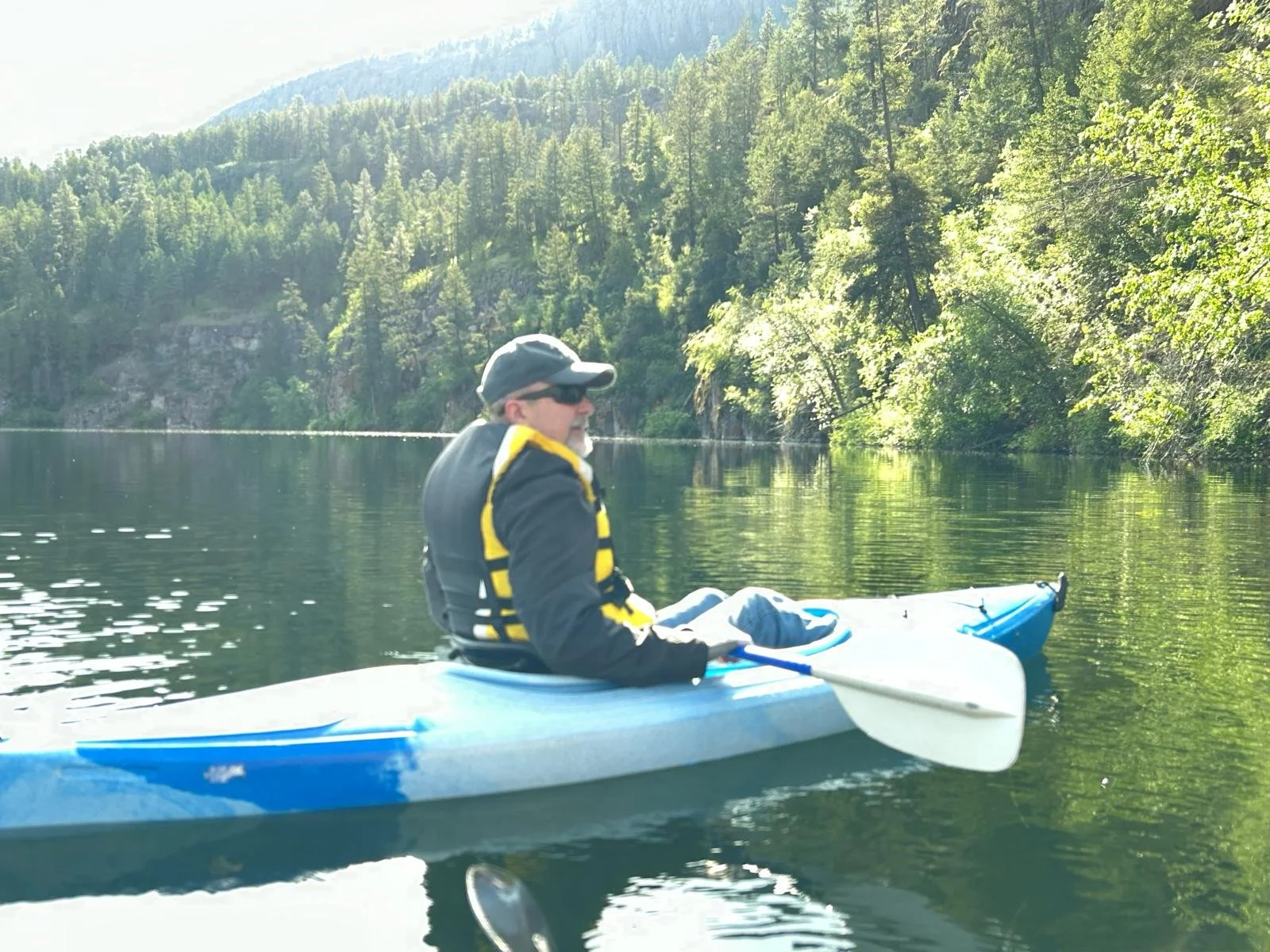 A man kayaking in a calm river surrounded by lush green trees and mountains.