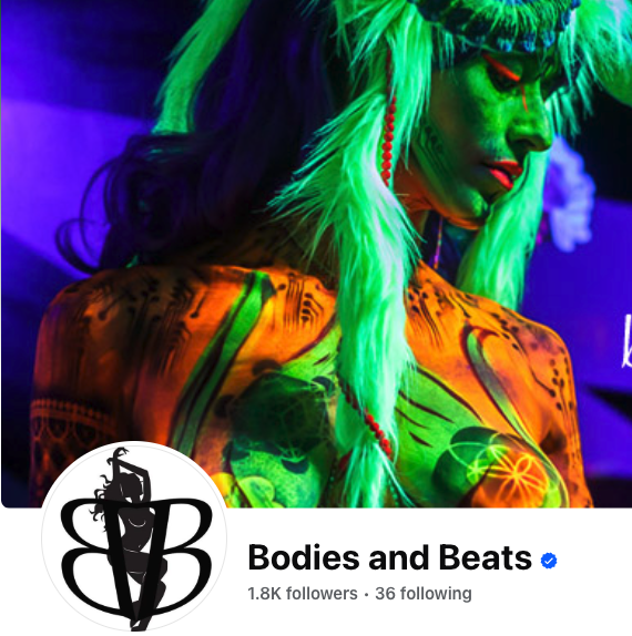 Person with bright green hair and elaborate costume on stage, illuminated by purple lighting.