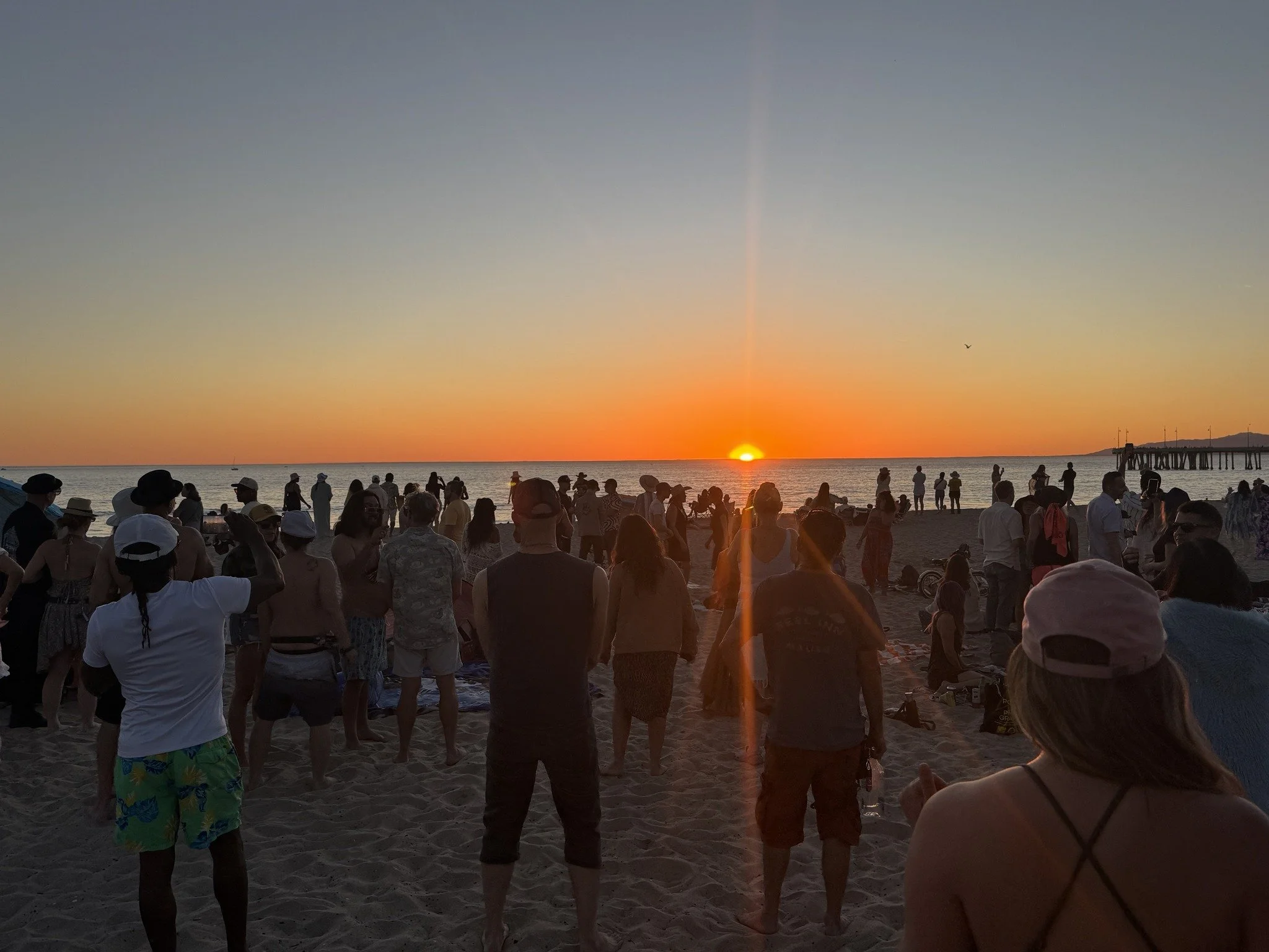 Crowd of people on the beach watching sunset over the ocean.