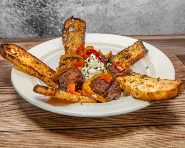 Plate with grilled meatballs, toasted bread slices, roasted peppers, and a dollop of sour cream garnished with herbs.