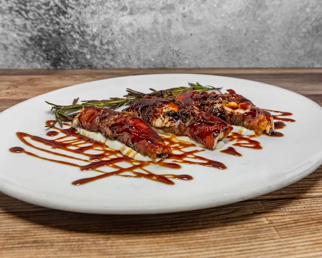 Baked stuffed zucchini topped with barbecue sauce, garnished with fresh rosemary, served on a white plate.