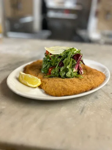 A plate with breaded fried fish fillet topped with lettuce and a lemon wedge.