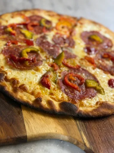 Close-up of a pizza with pepperoni, green peppers, and red peppers on a wooden serving board.