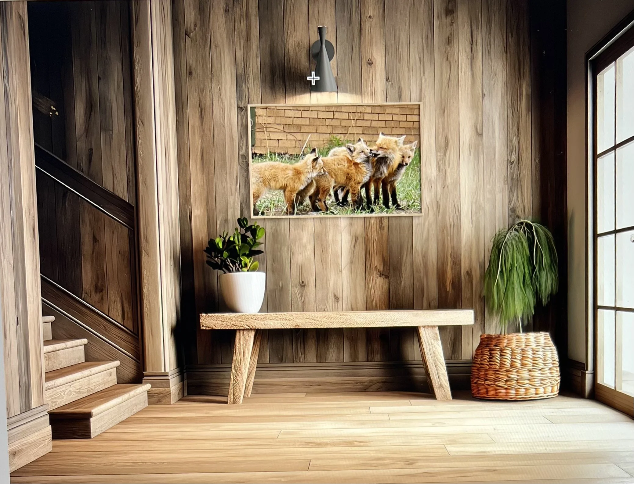 A wooden wall with a framed picture of a group of foxes, a small staircase, a white potted plant, and a wicker stool inside a cozy room with natural light.