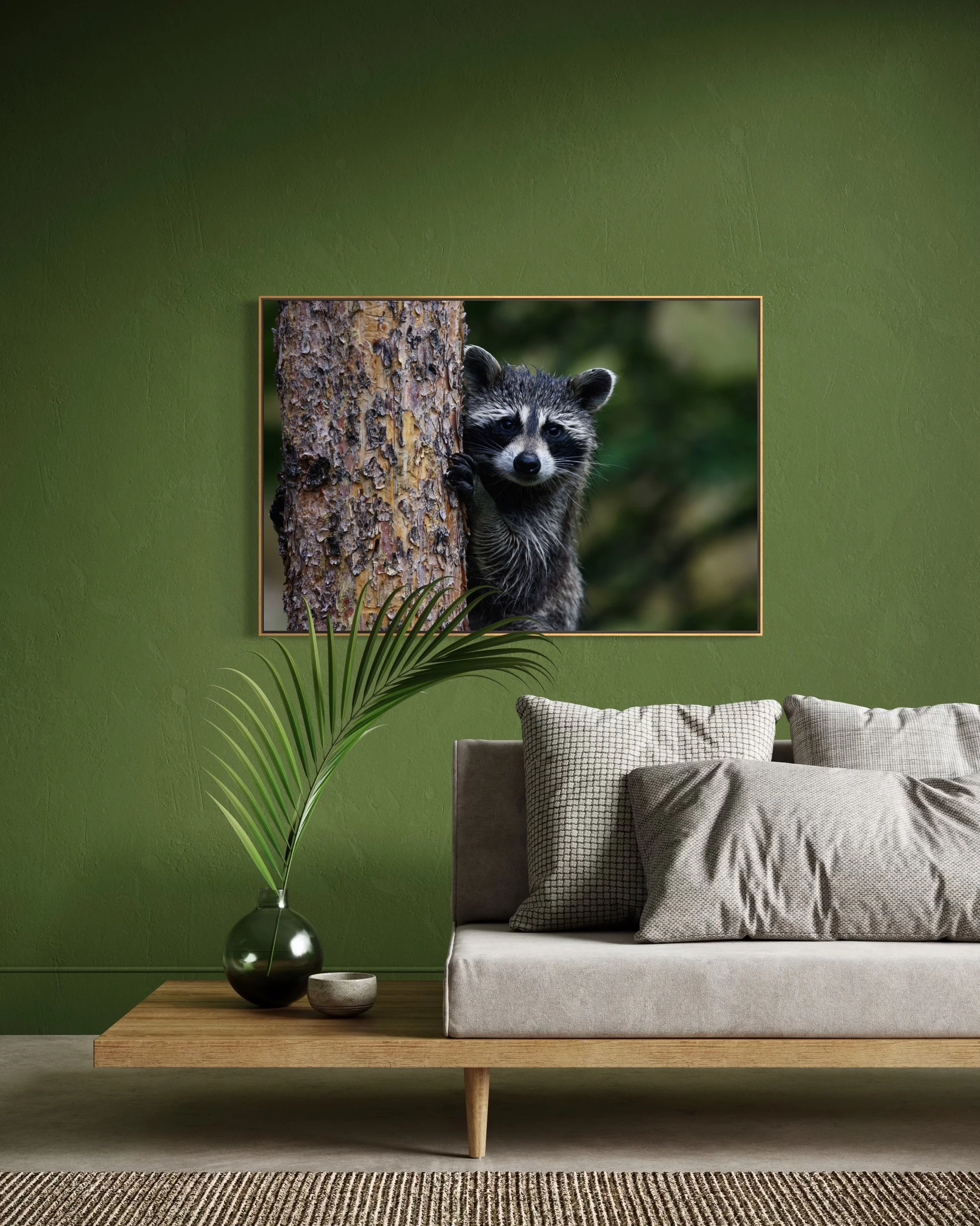 Living room with a beige sofa, a green wall, a wooden coffee table with two pottery bowls and a black vase with a potted plant, and a framed photo of a raccoon on the wall.