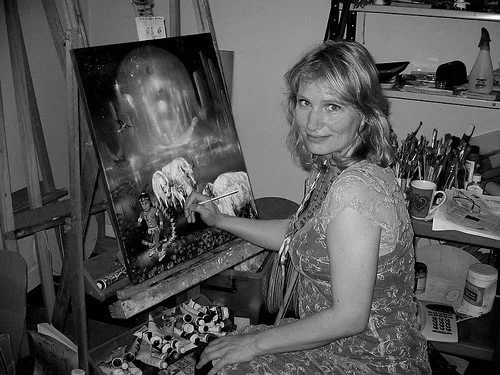 Woman painting a cosmic scene with a moon and a landscape on a canvas in an art studio.