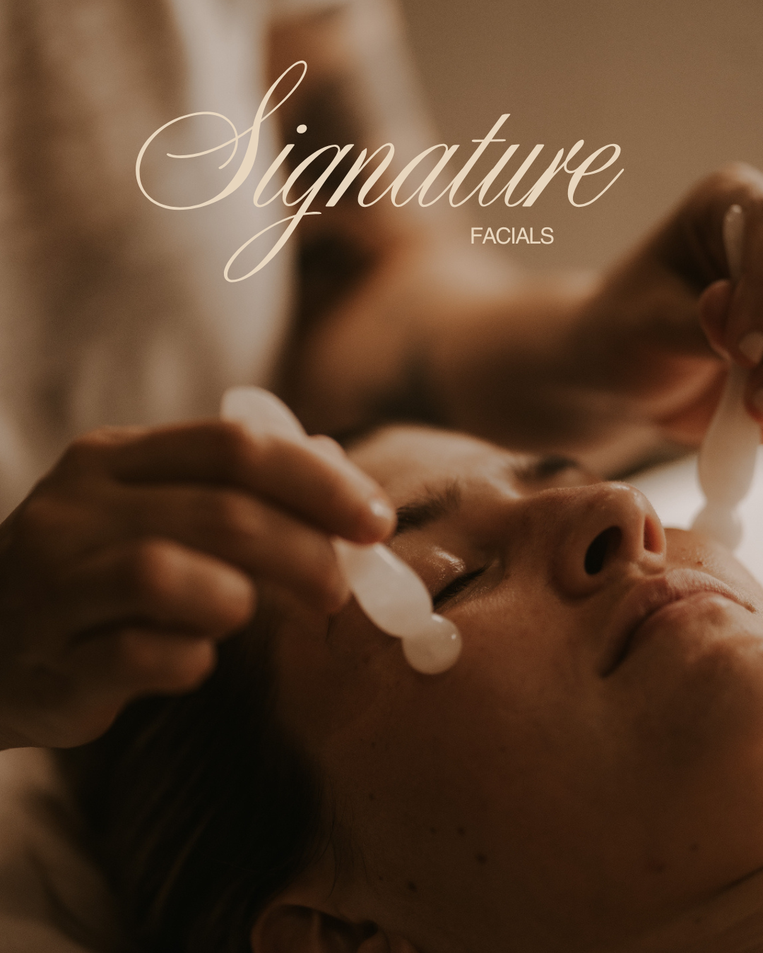 A woman receiving a facial treatment with jade rollers applied to her face in a spa setting.