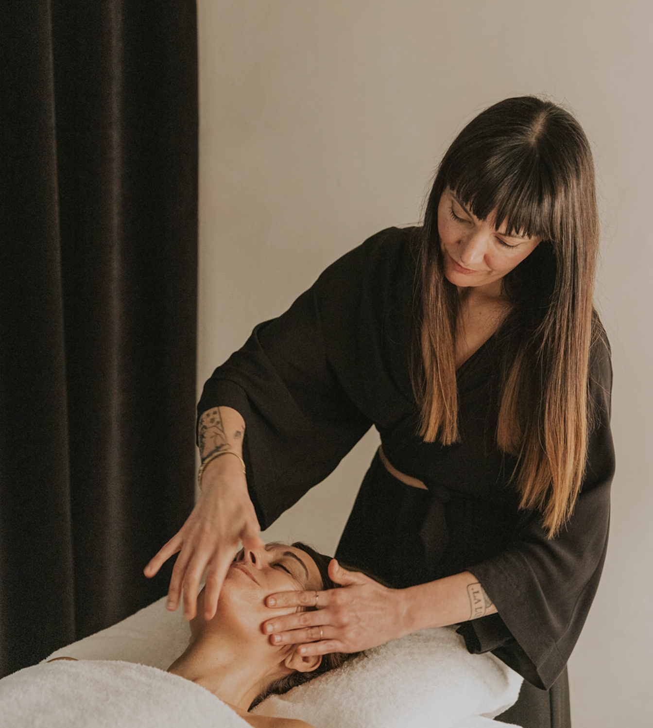 A woman receiving facial massage from a therapist in a spa or skincare clinic.