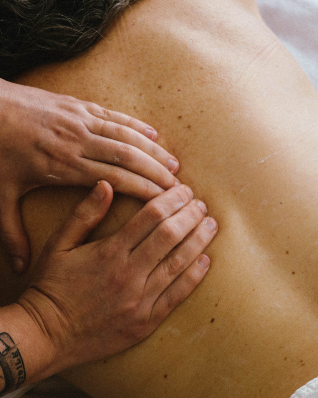 Close-up of a person's back being massaged or padded, focusing on the upper back and shoulder area.
