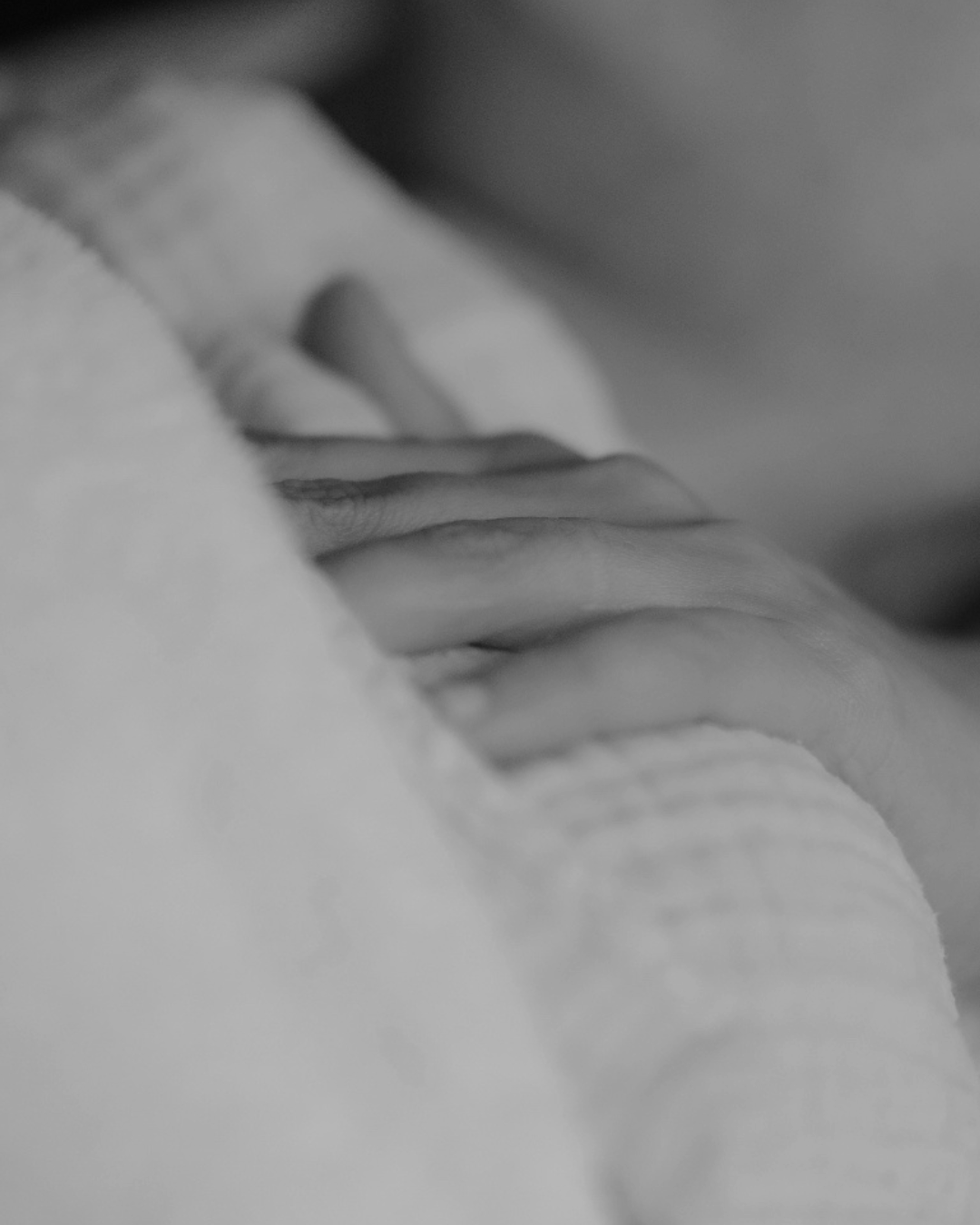 Close-up of two hands gently touching or holding each other in black and white.