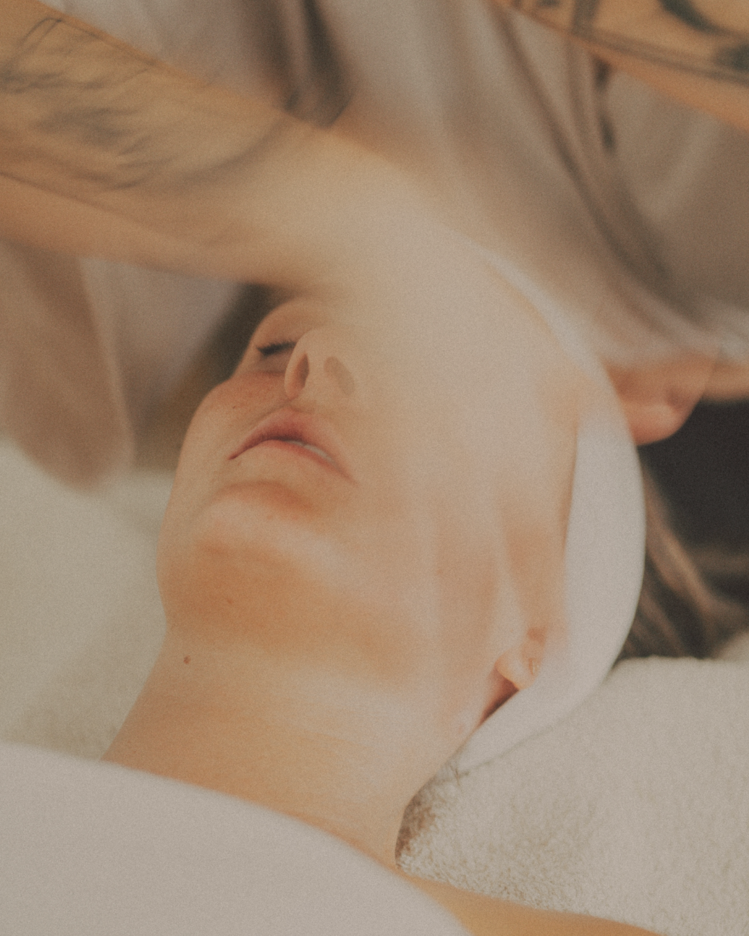 A woman lying on her back with eyes closed, receiving a facial massage in a spa setting.